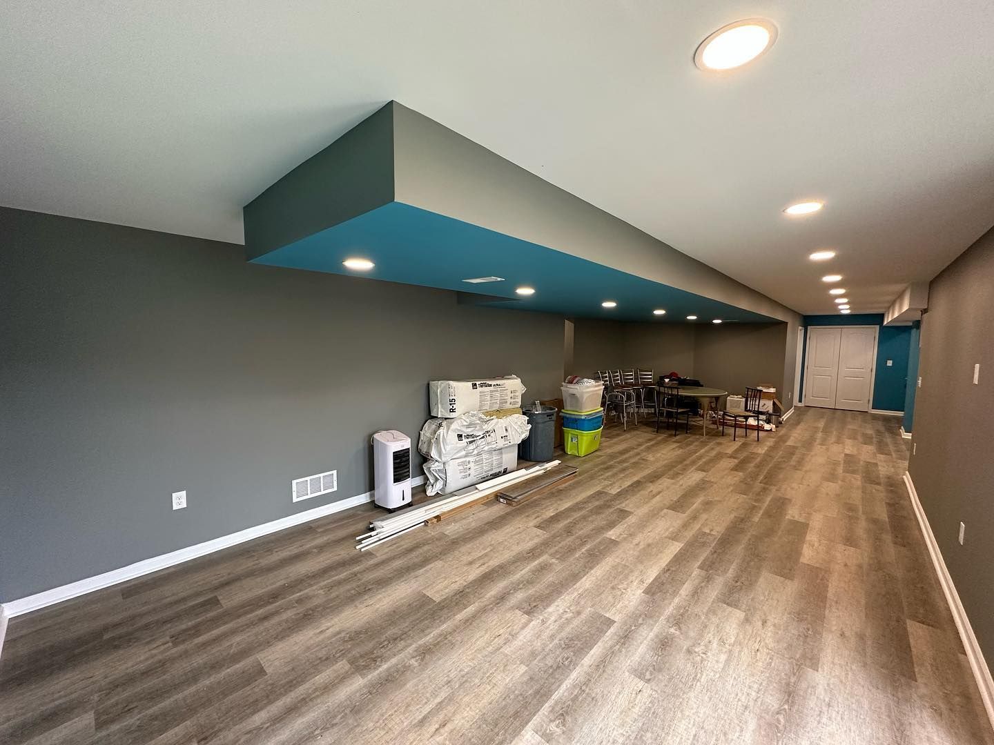 Basement with gray walls, wood-look flooring, and a blue ceiling section.  Items against walls.