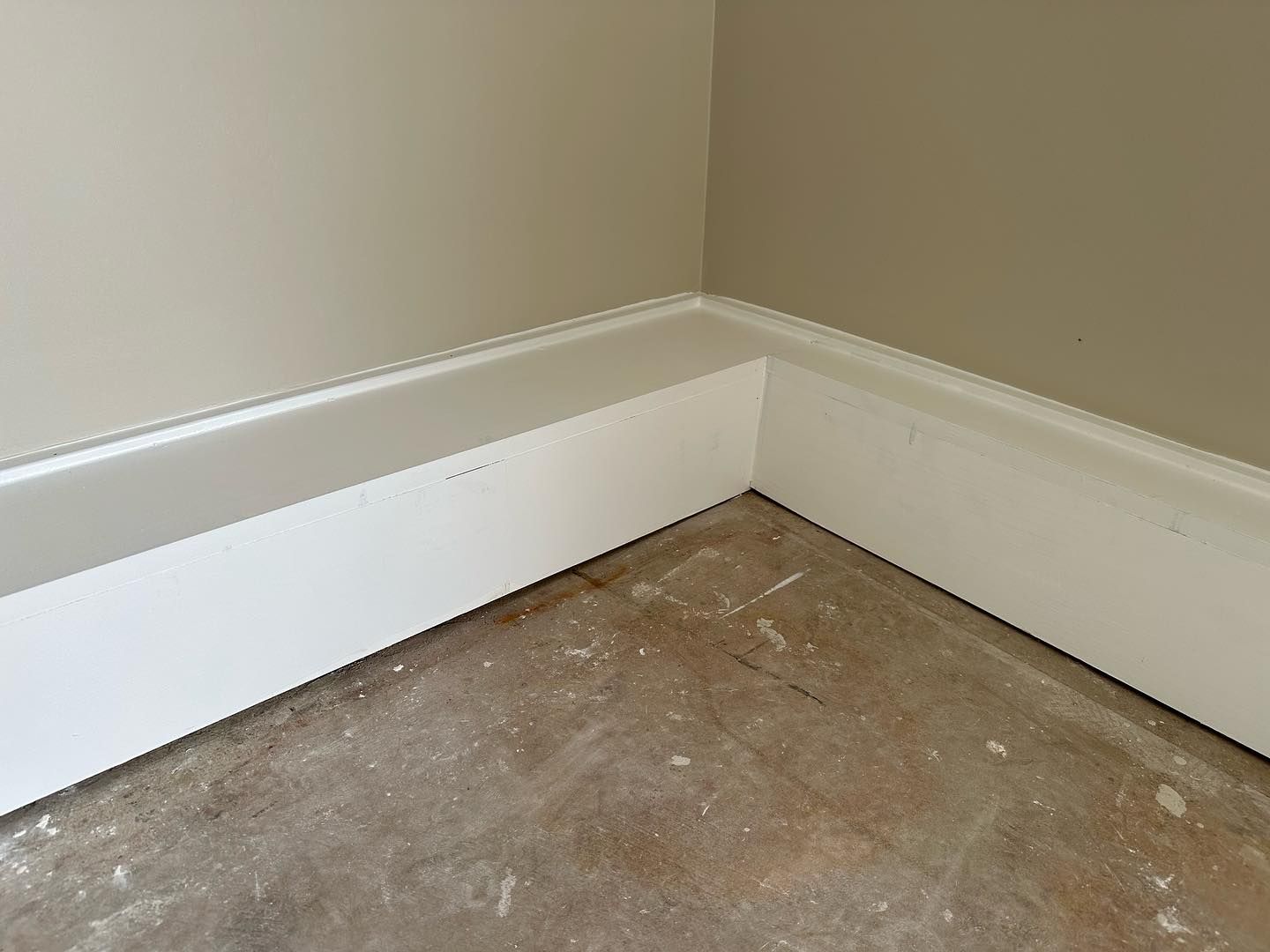 A corner of a room with a white molding and a concrete floor.