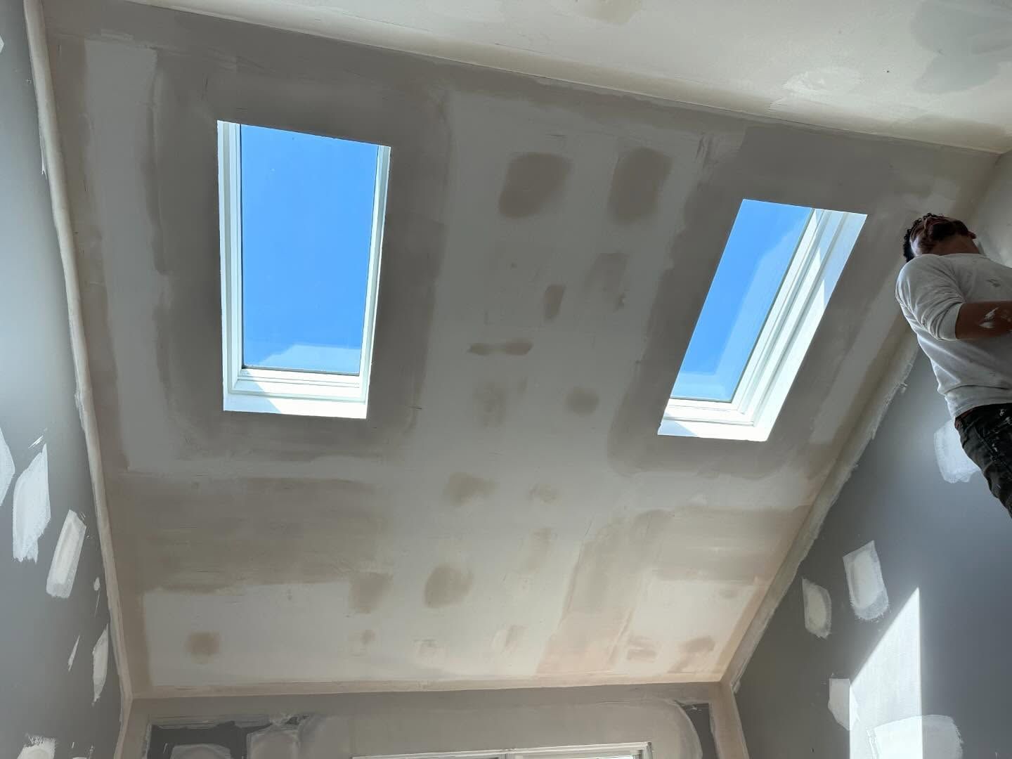 A man is standing in a room with two skylights in the ceiling.