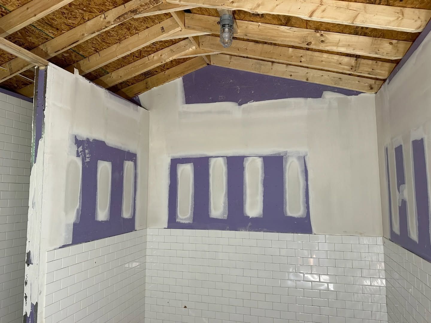 A bathroom under construction with purple drywall and white tiles.