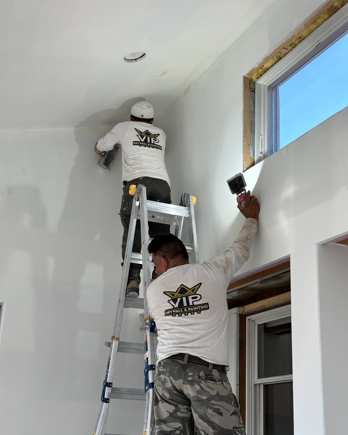 Two men are standing on a ladder painting a wall.
