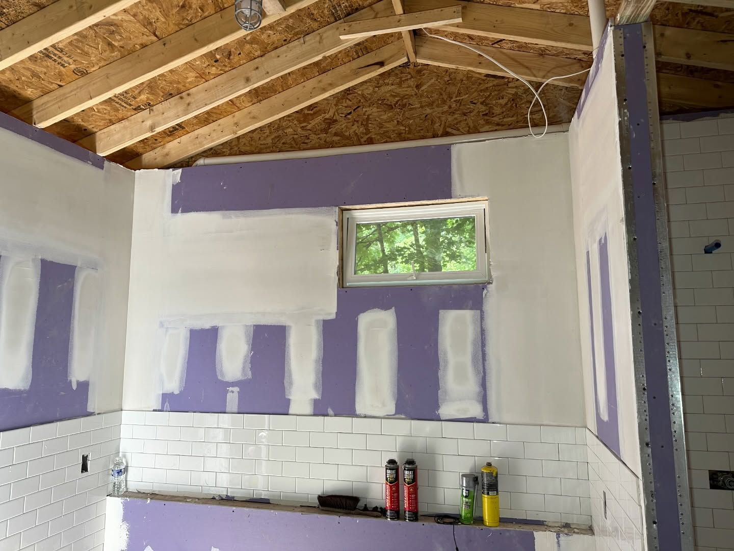 A kitchen under construction with purple and white walls and a window.