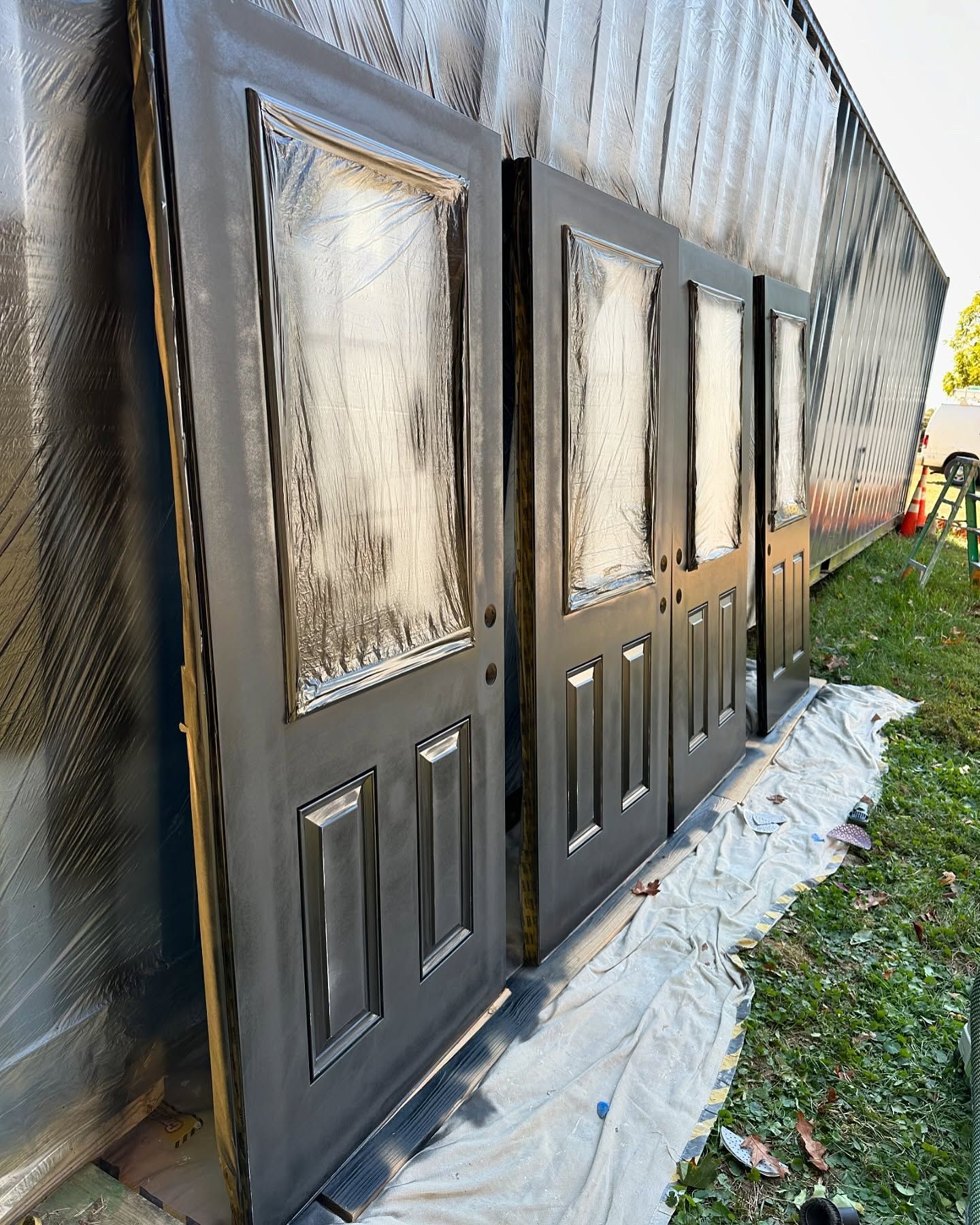 A row of doors sitting on top of a tarp in the grass.