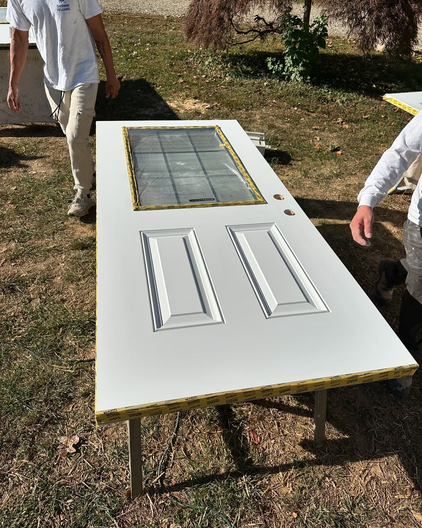 A man is standing next to a long white door in the grass.