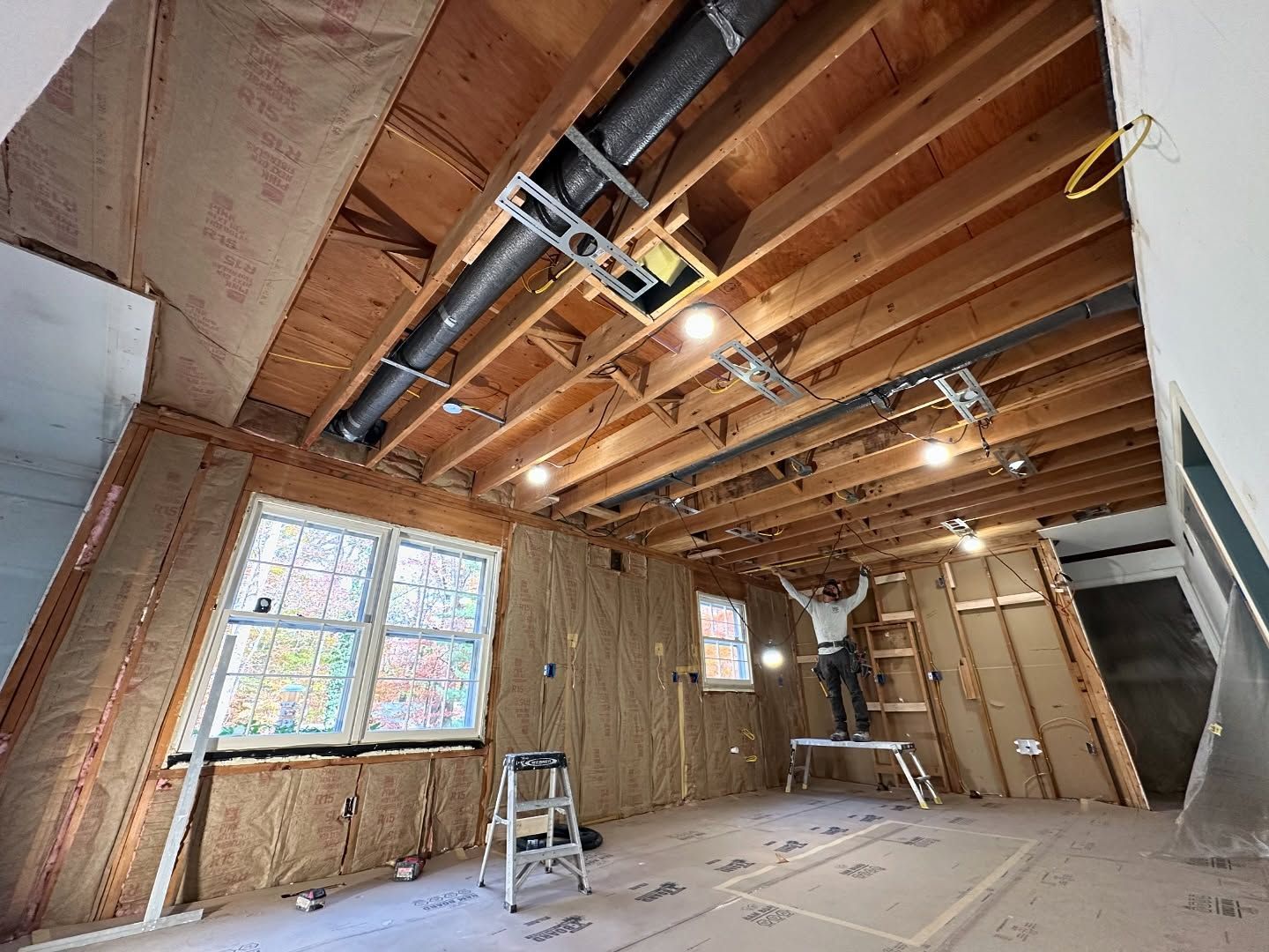 A man is standing on a ladder in a room under construction.