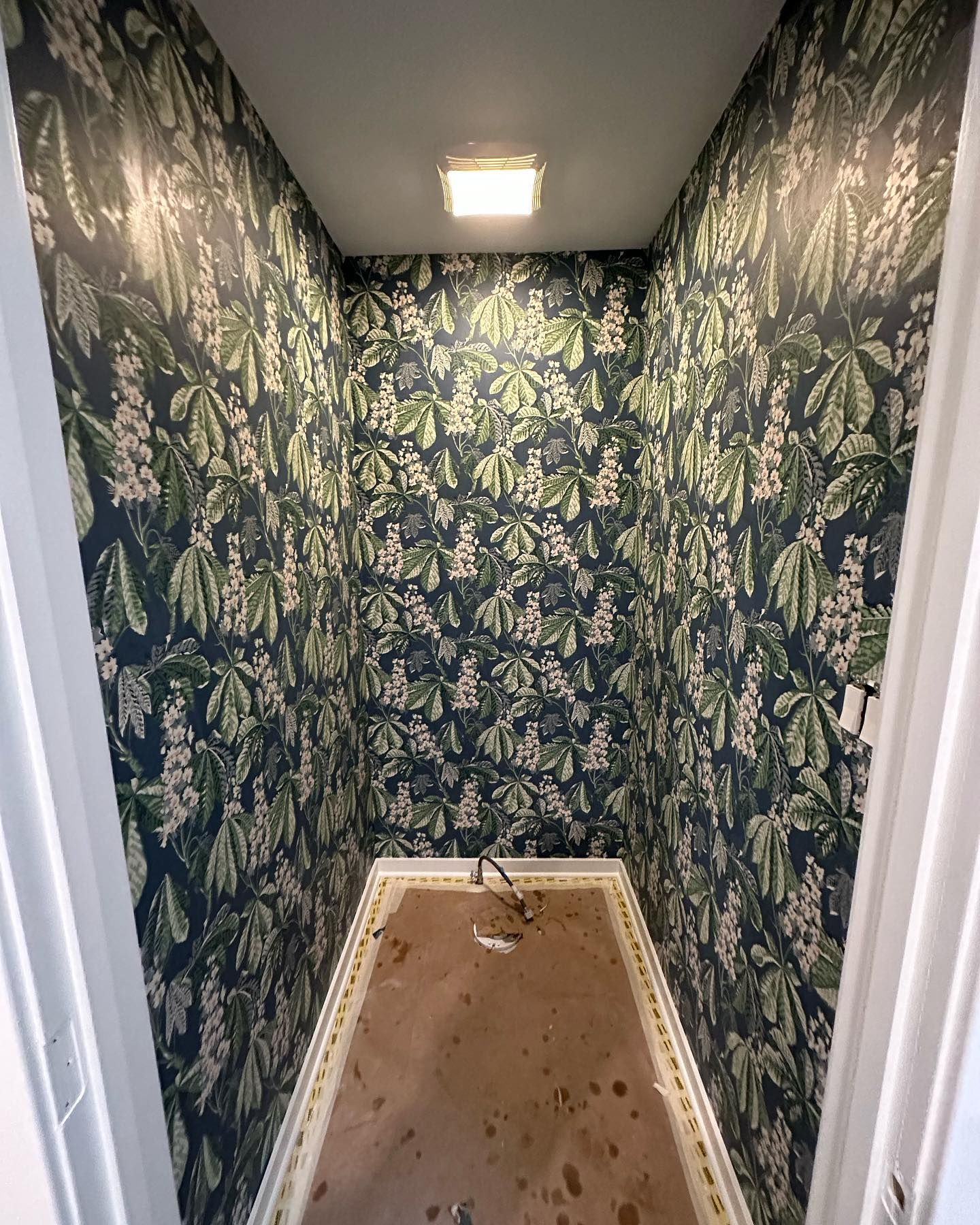 A small room with a floral wallpaper on the walls and a light on the ceiling.