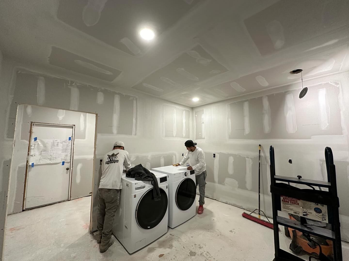 Two men are working in a laundry room with a washer and dryer.