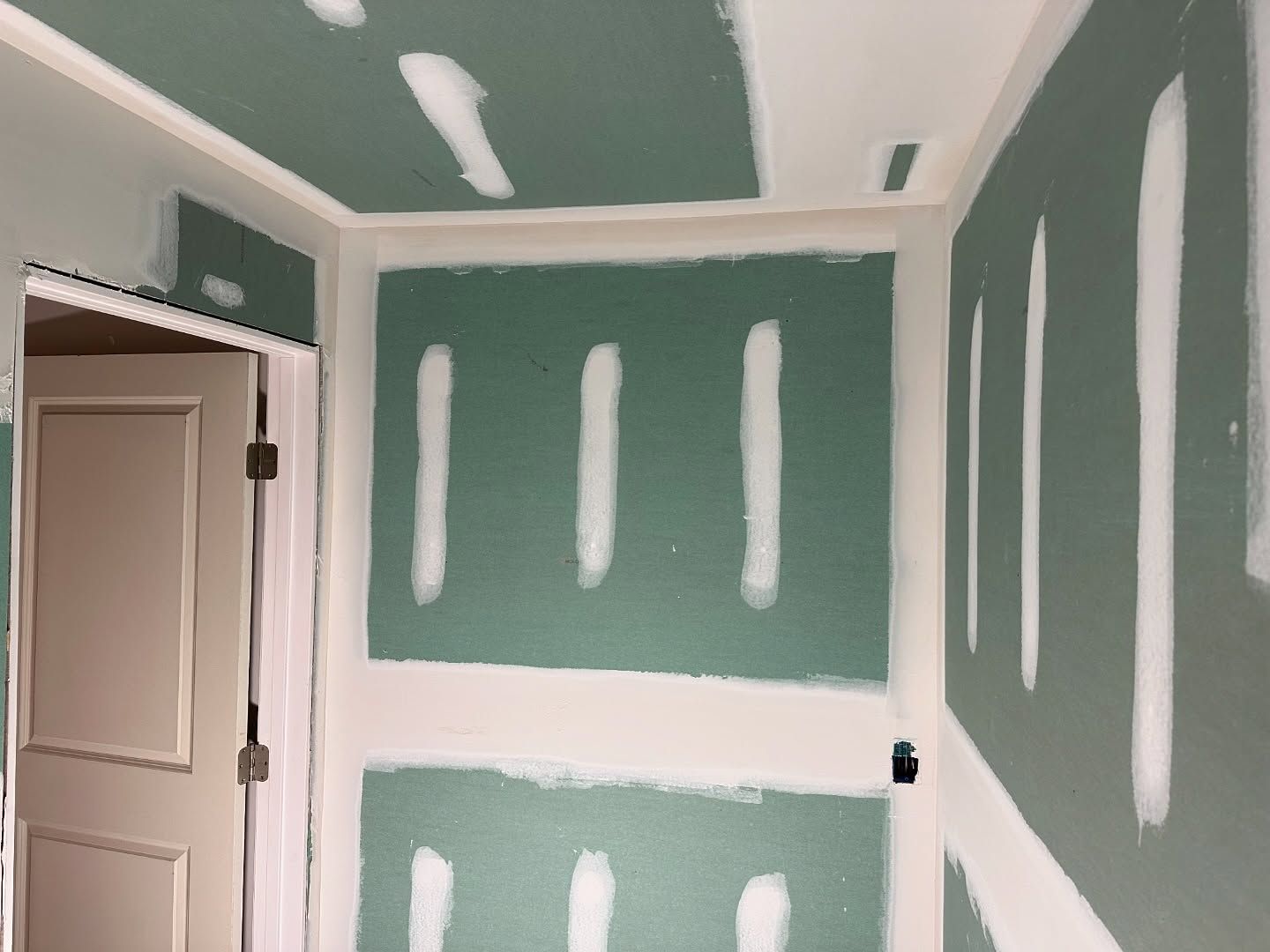 A room with green and white drywall and a door.
