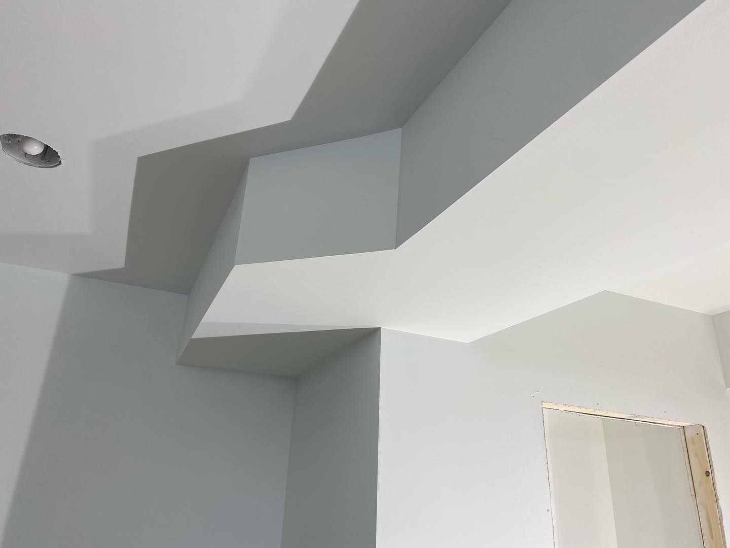 A room with white walls and a ceiling that looks like a staircase.