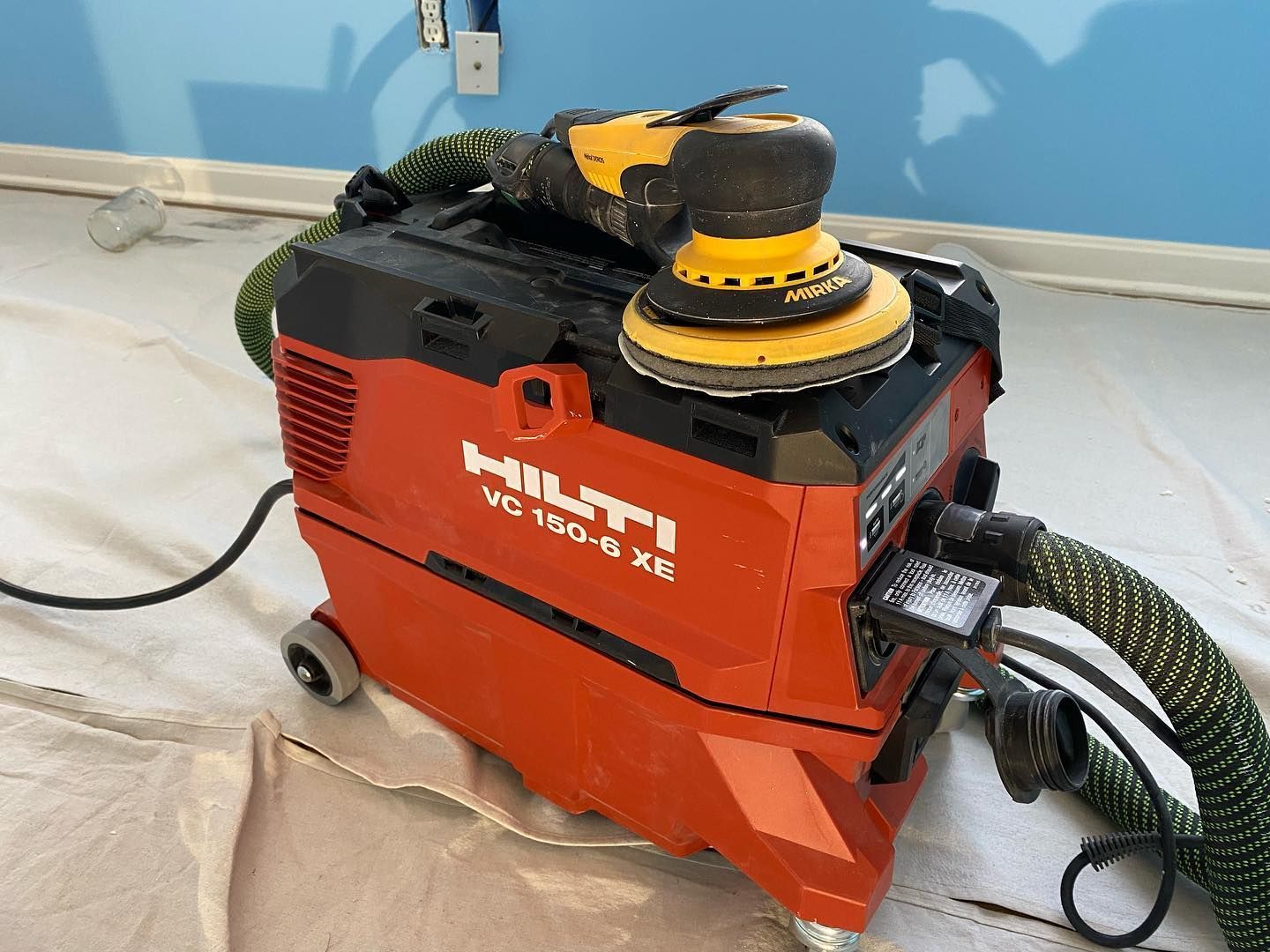 A red vacuum cleaner with a yellow sander on top of it.