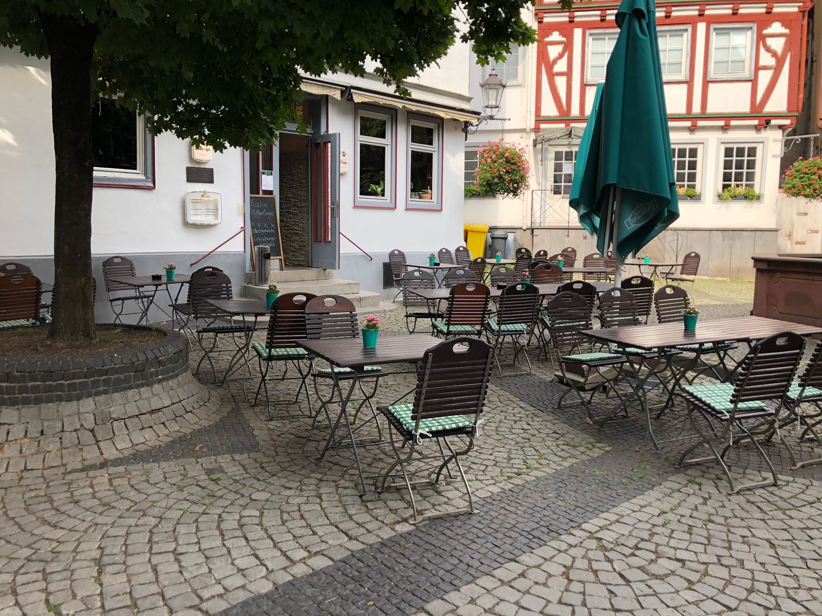 Eine Terrasse mit Tischen und Stühlen und einem Sonnenschirm vor einem Gebäude.
