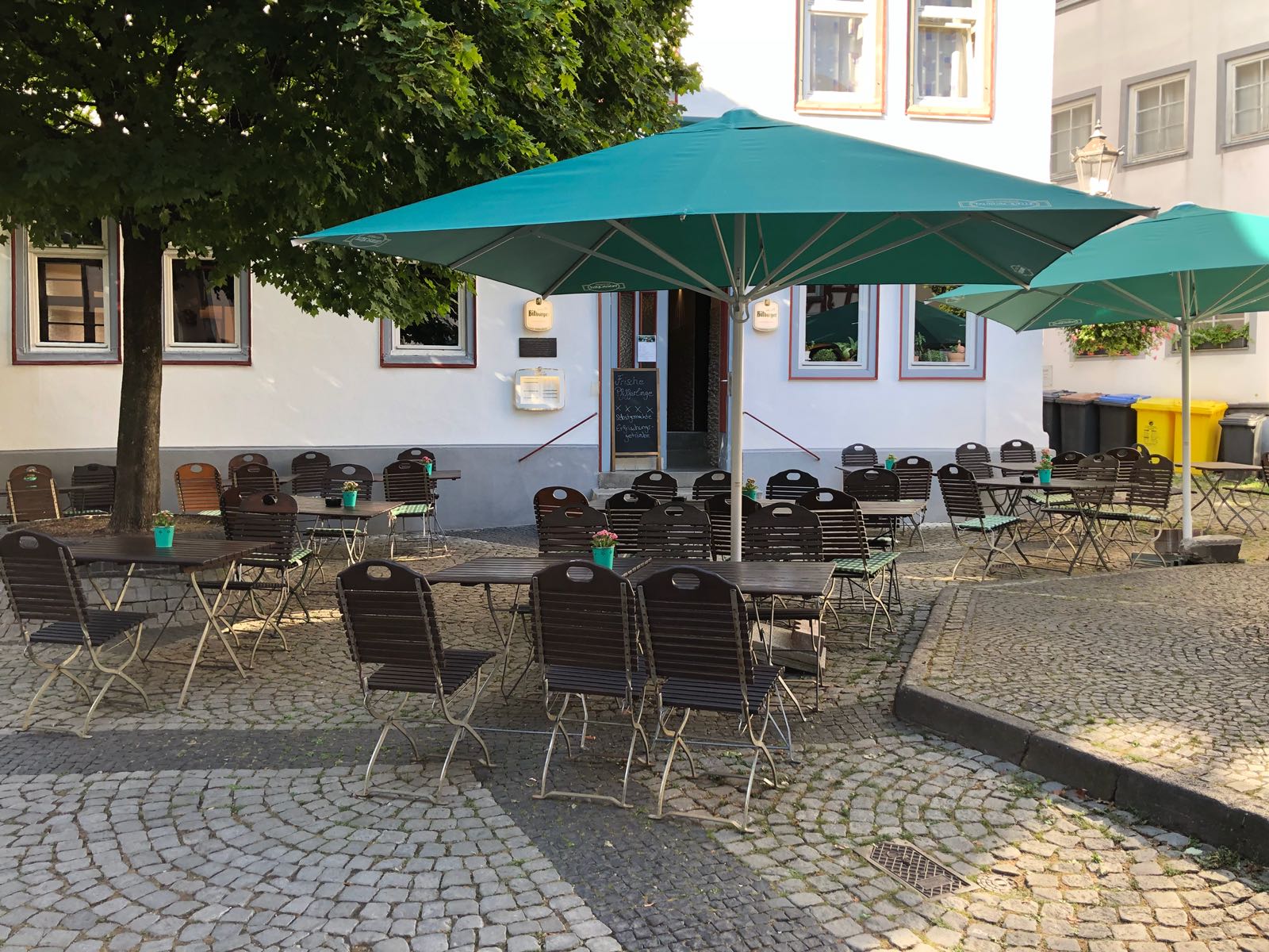 Eine Terrasse mit Tischen, Stühlen und Sonnenschirmen vor einem Gebäude