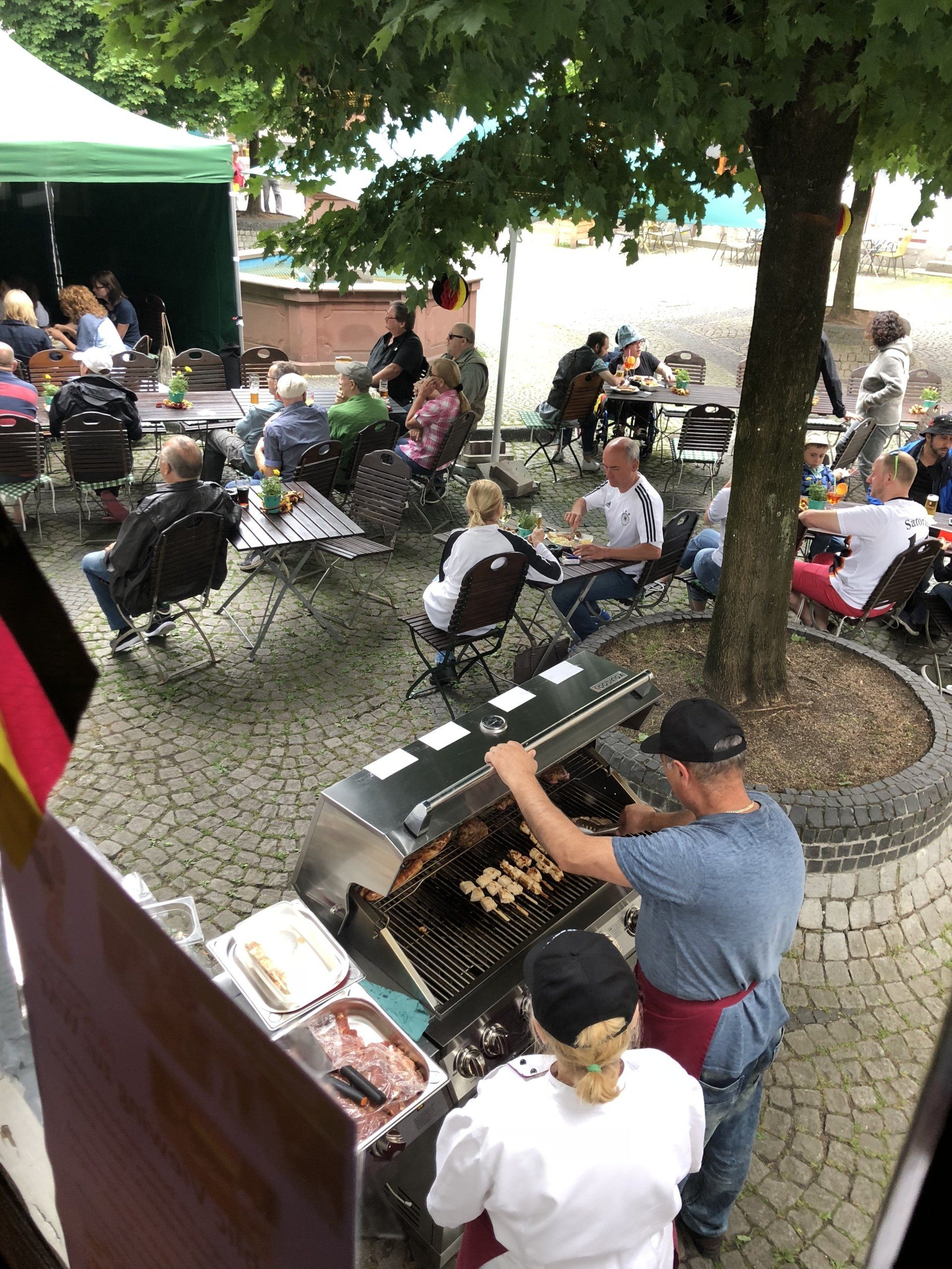 Eine Gruppe von Menschen sitzt an Tischen unter einem Baum in einem Park.