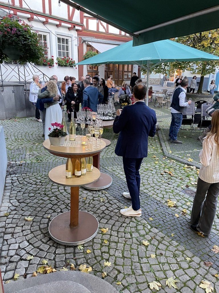 Eine Gruppe von Menschen steht auf einer Kopfsteinpflasterstraße um Tische herum.