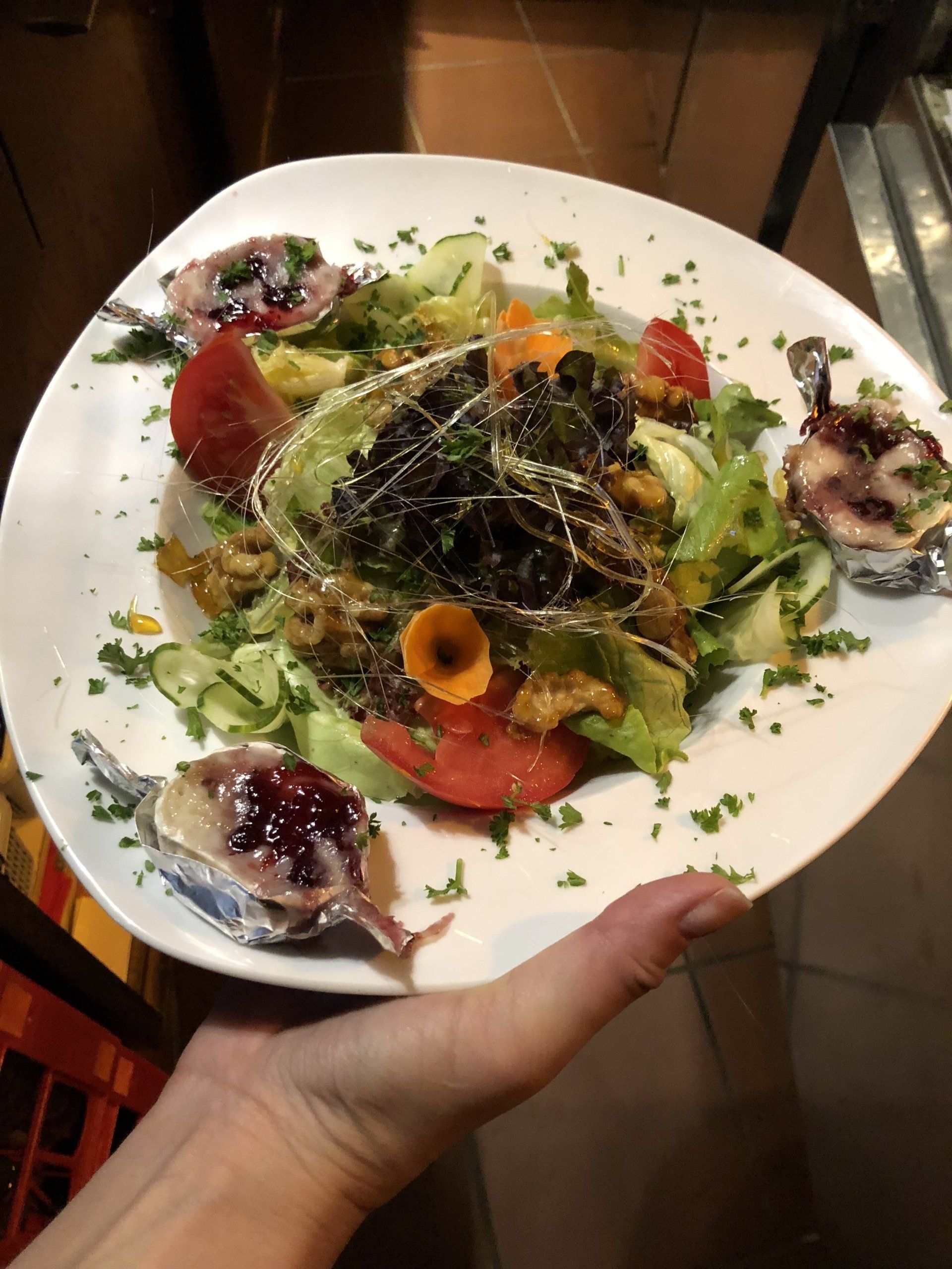 Eine Person hält einen weißen Teller mit einem Salat darauf