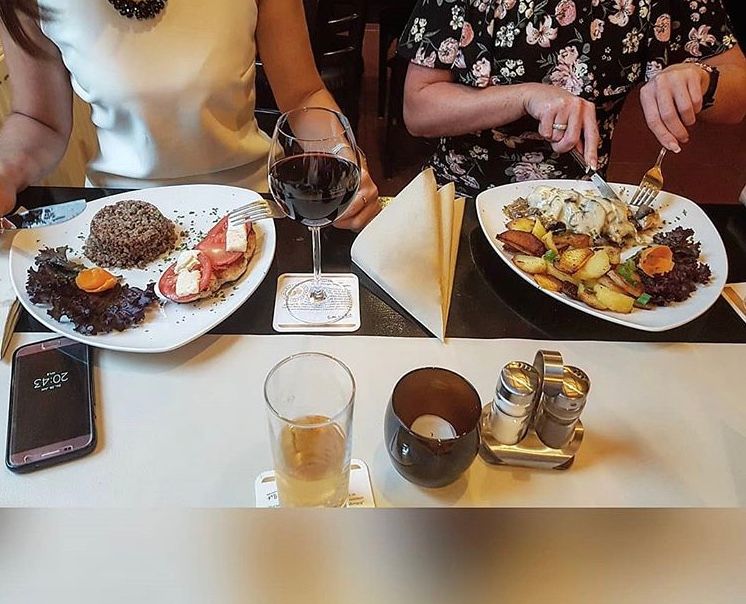 Zwei Frauen sitzen an einem Tisch mit Tellern voller Essen und einem Glas Wein