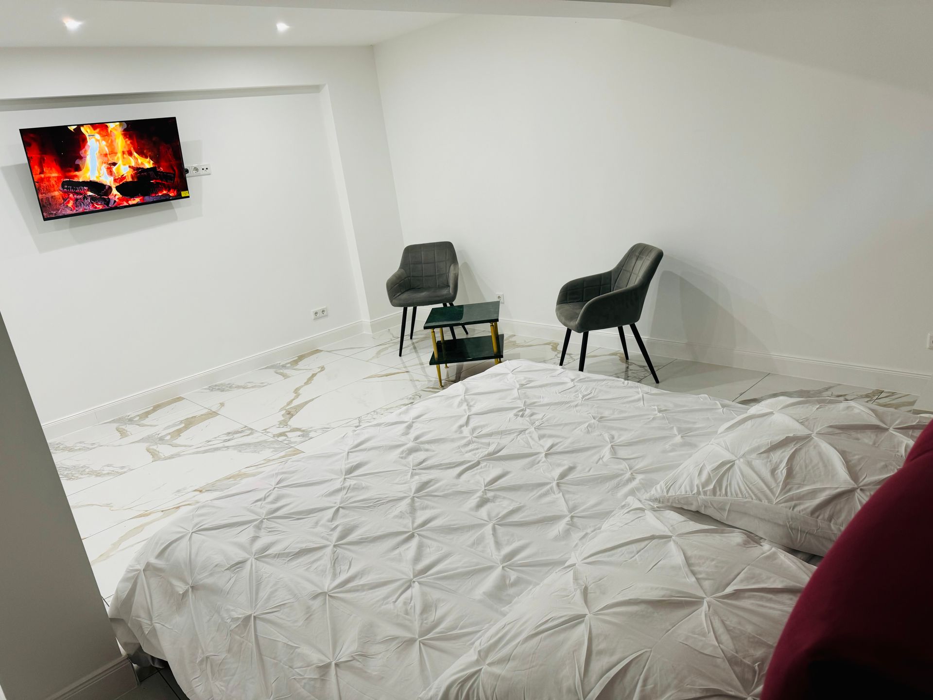 Ein Schlafzimmer mit einem Bett, Stühlen, einem Fernseher und einem Kamin.