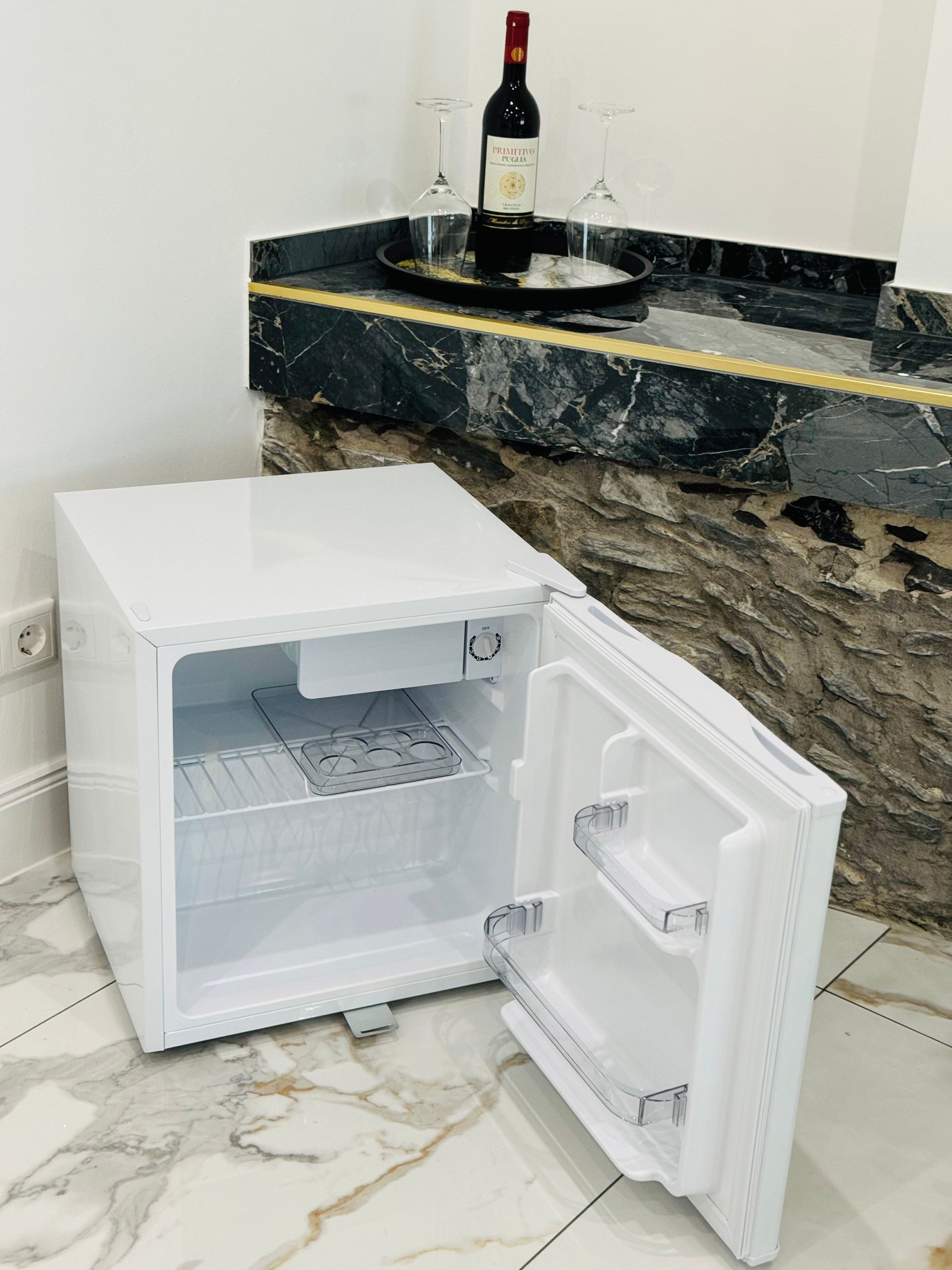 Ein kleiner weißer Kühlschrank mit offener Tür und einer Flasche Wein darin.