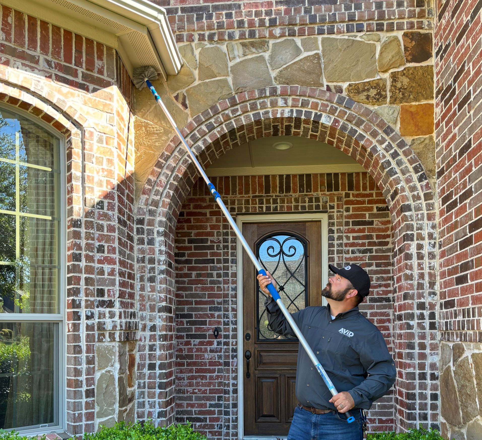 A man is cleaning the gutters of a brick house with a long pole.