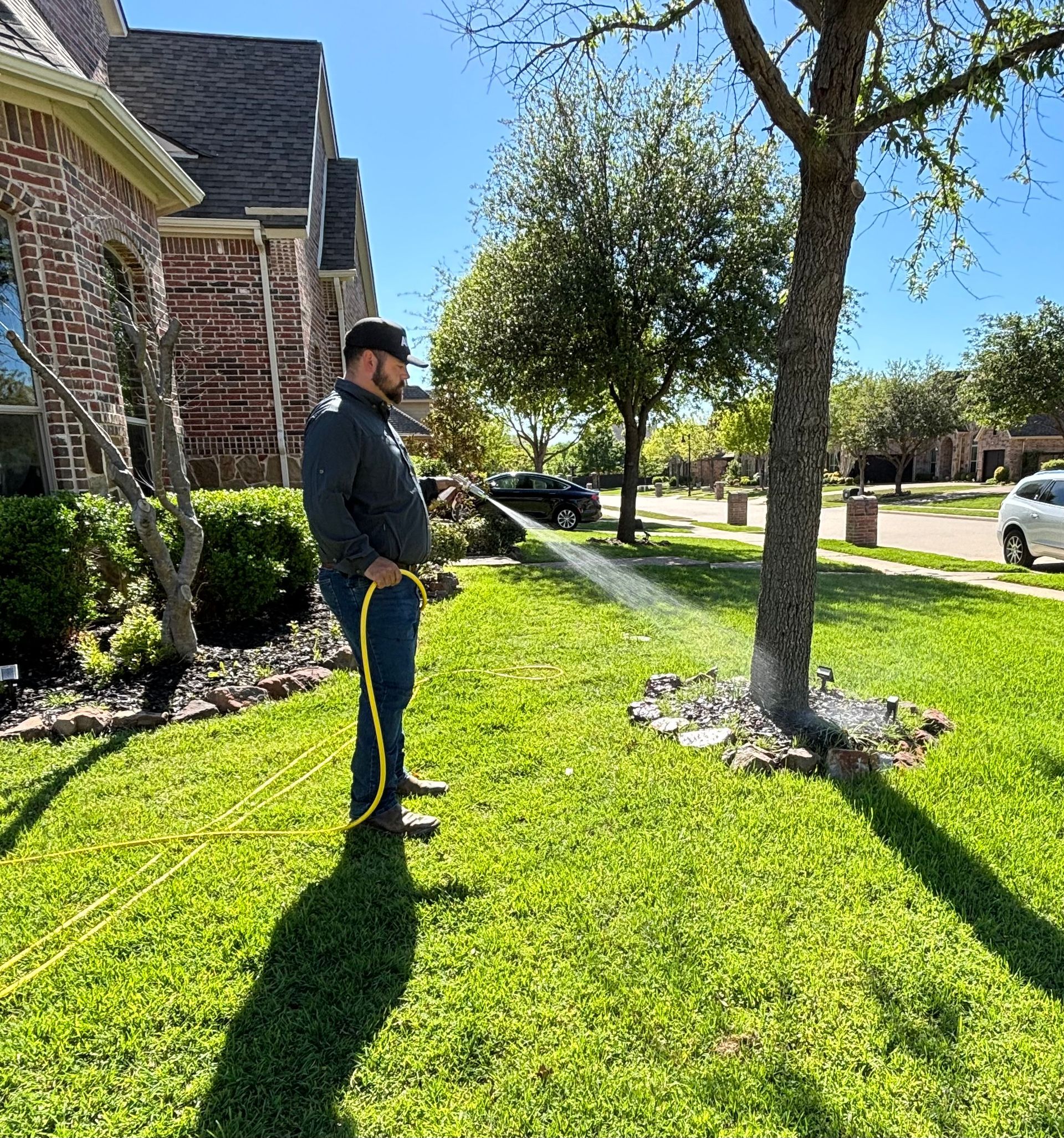 A man is watering a lawn with a hose in front of a house.