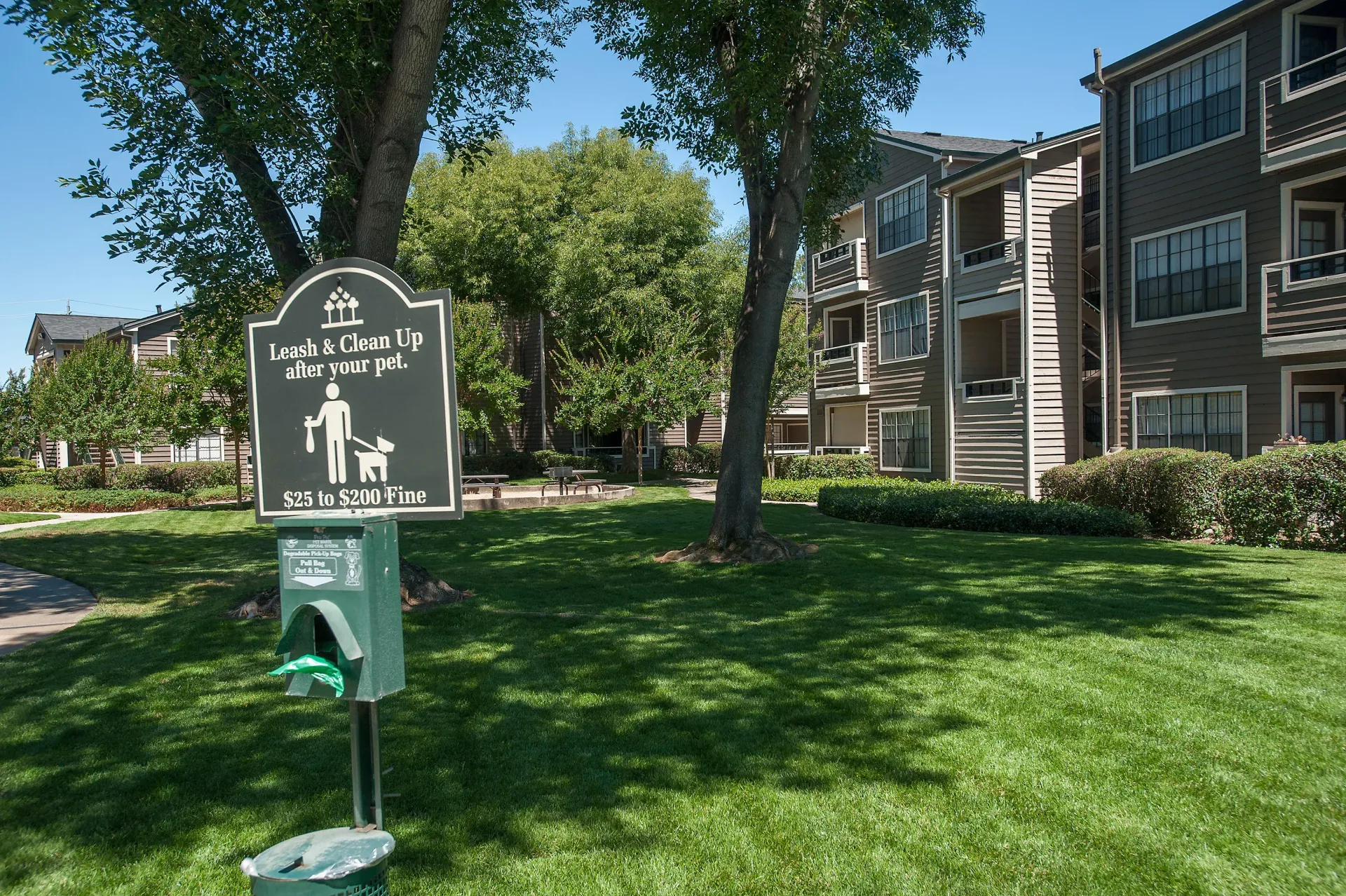 Apartment community courtyard with a pet leash-and-clean-up sign in front of a multi-unit building.