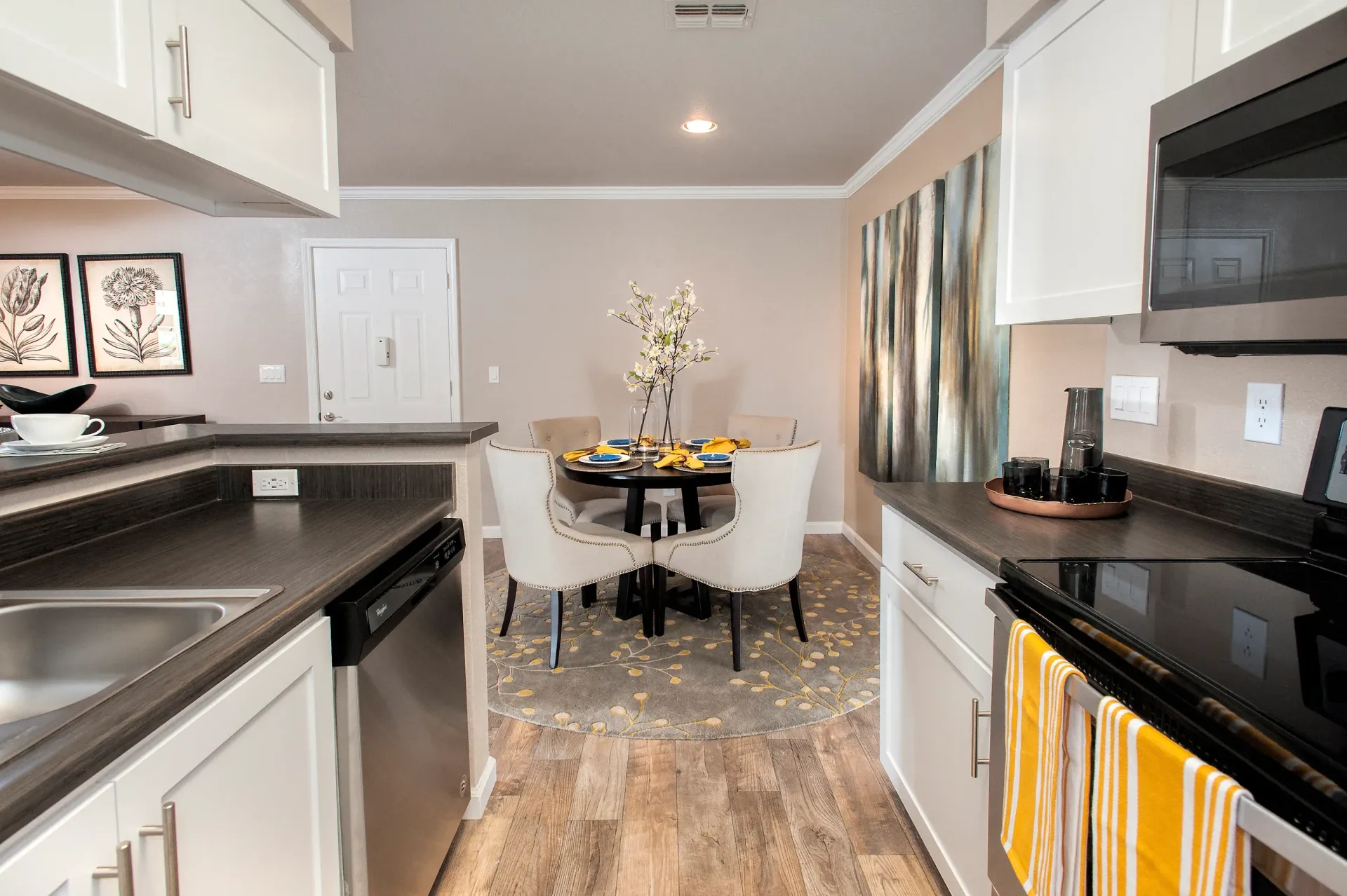 Open kitchen with white cabinets, dark countertops, stainless appliances, and a round dining table.