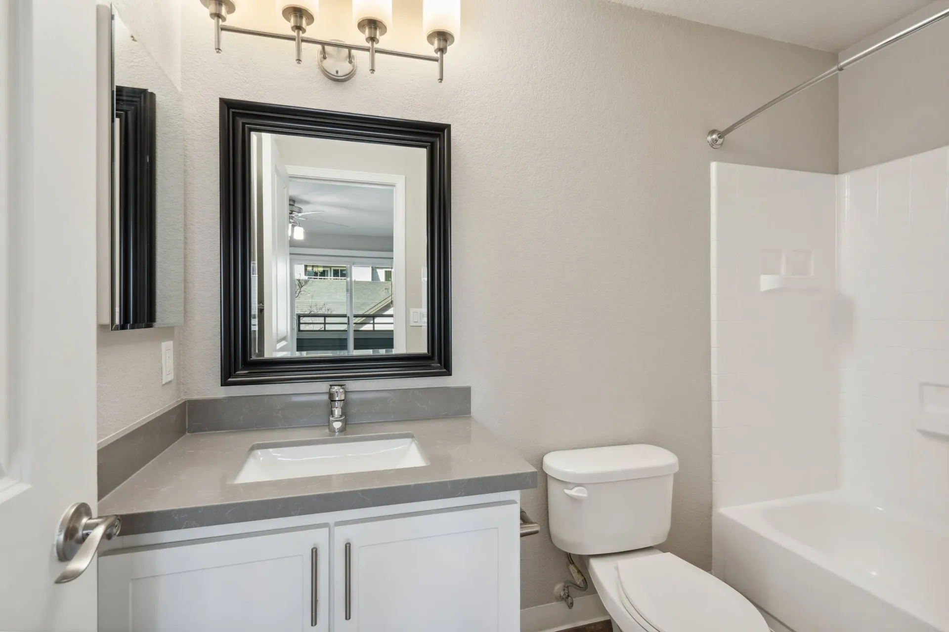 Bathroom in an apartment with gray countertop, white vanity, mirror, toilet, and tub/shower.
