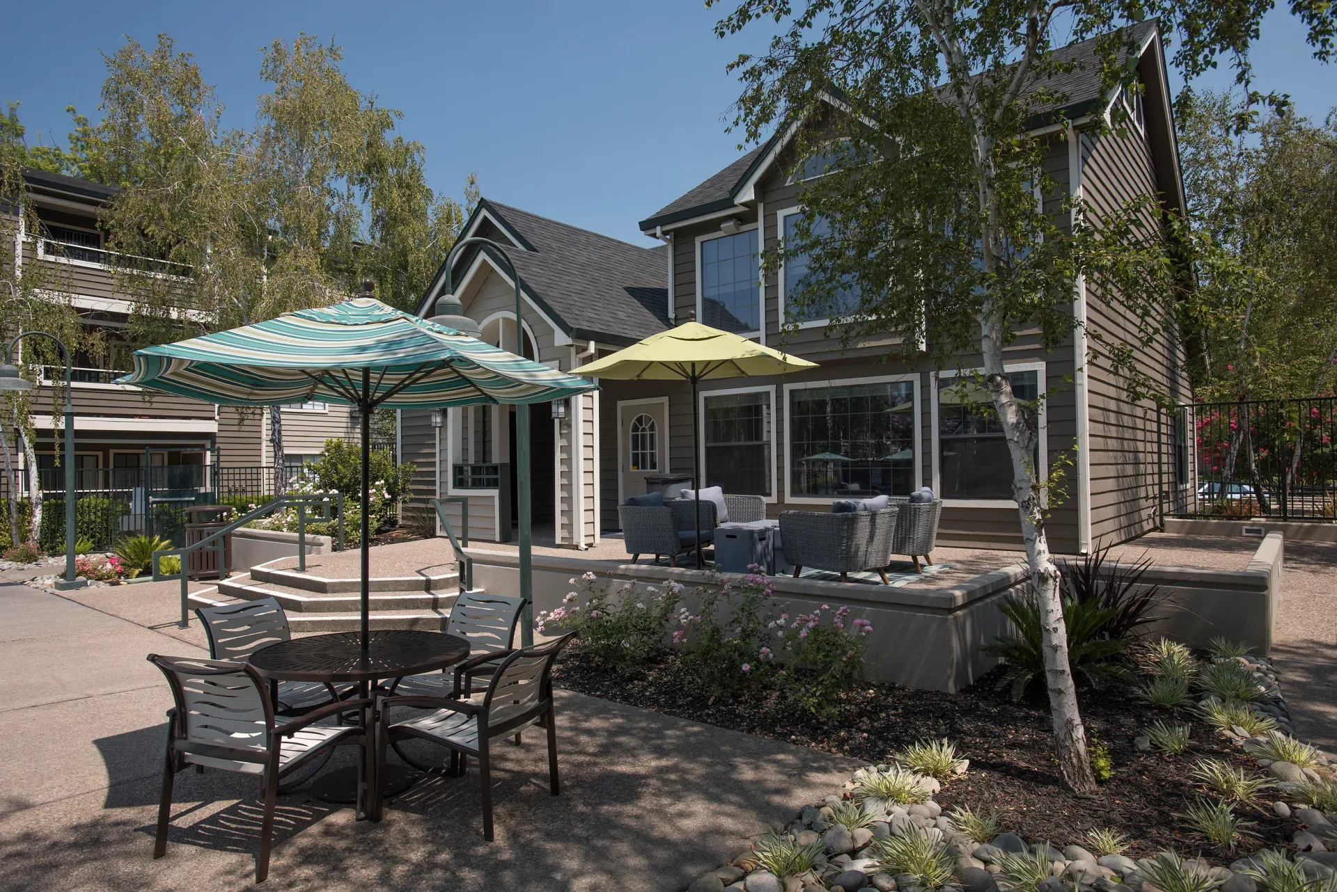 Exterior communal courtyard with patio furniture and umbrellas near an apartment building.