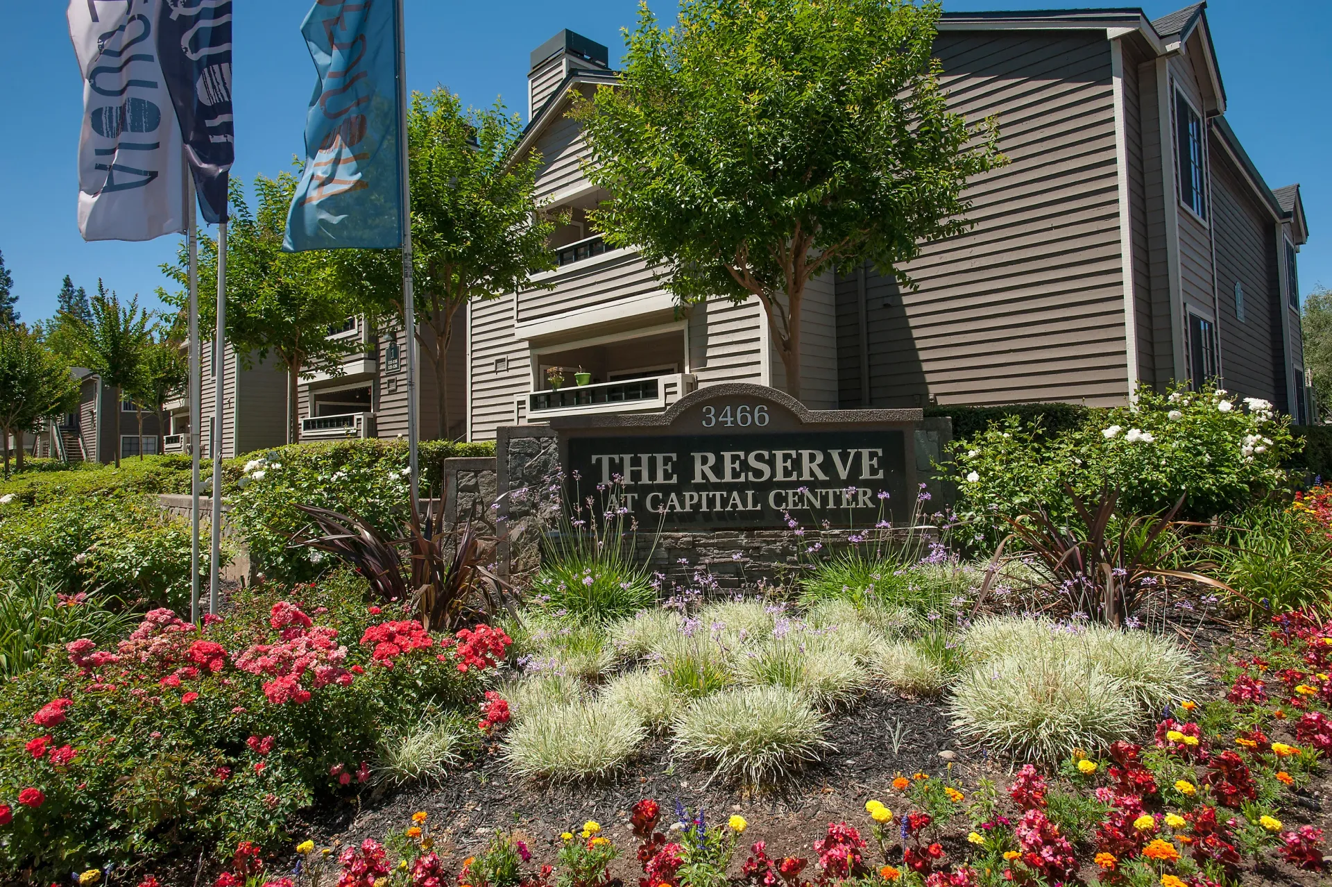 Exterior view of a multifamily community entrance with landscaping and a stone sign.
