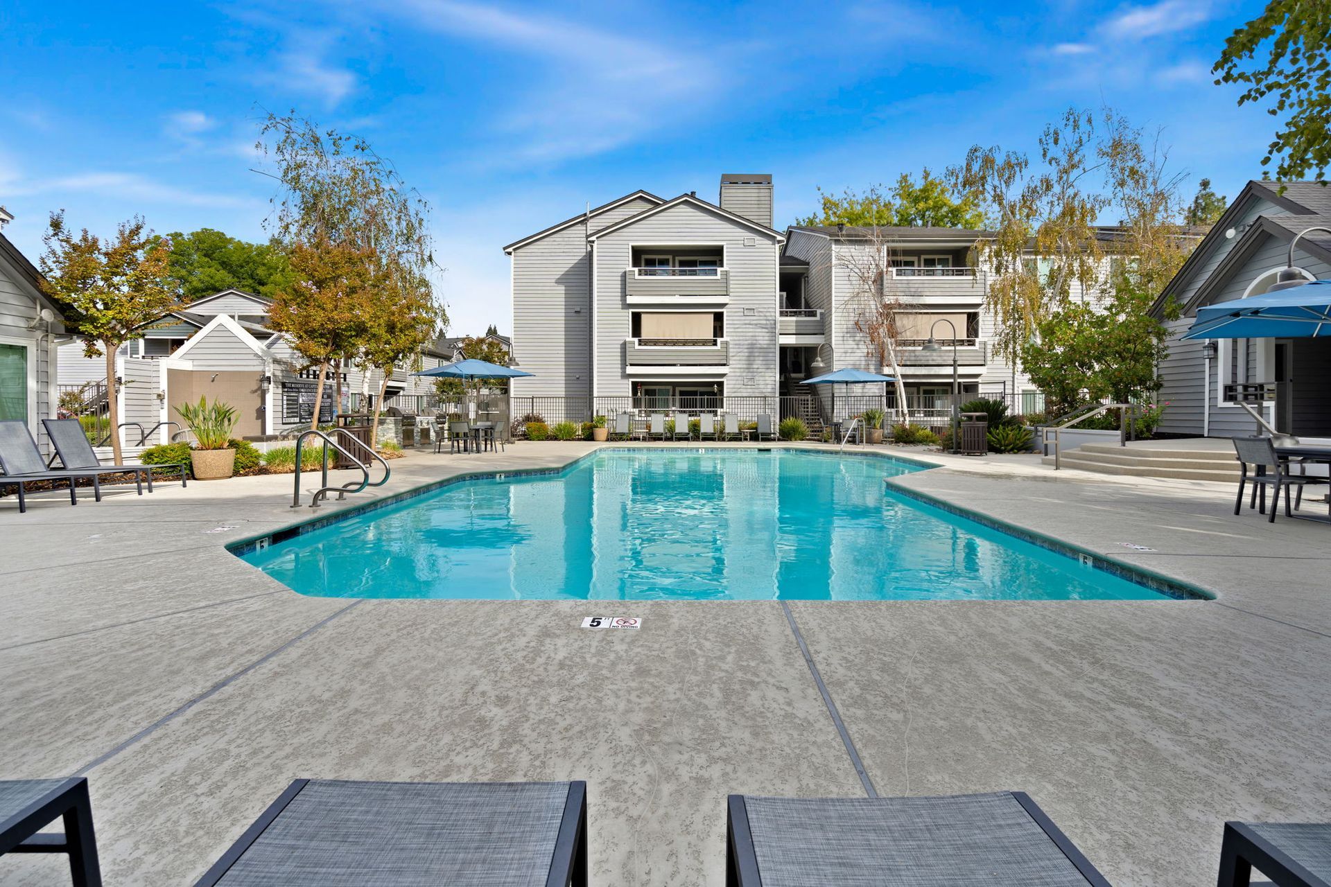 Outdoor community pool with lounge chairs and apartment buildings in the background.