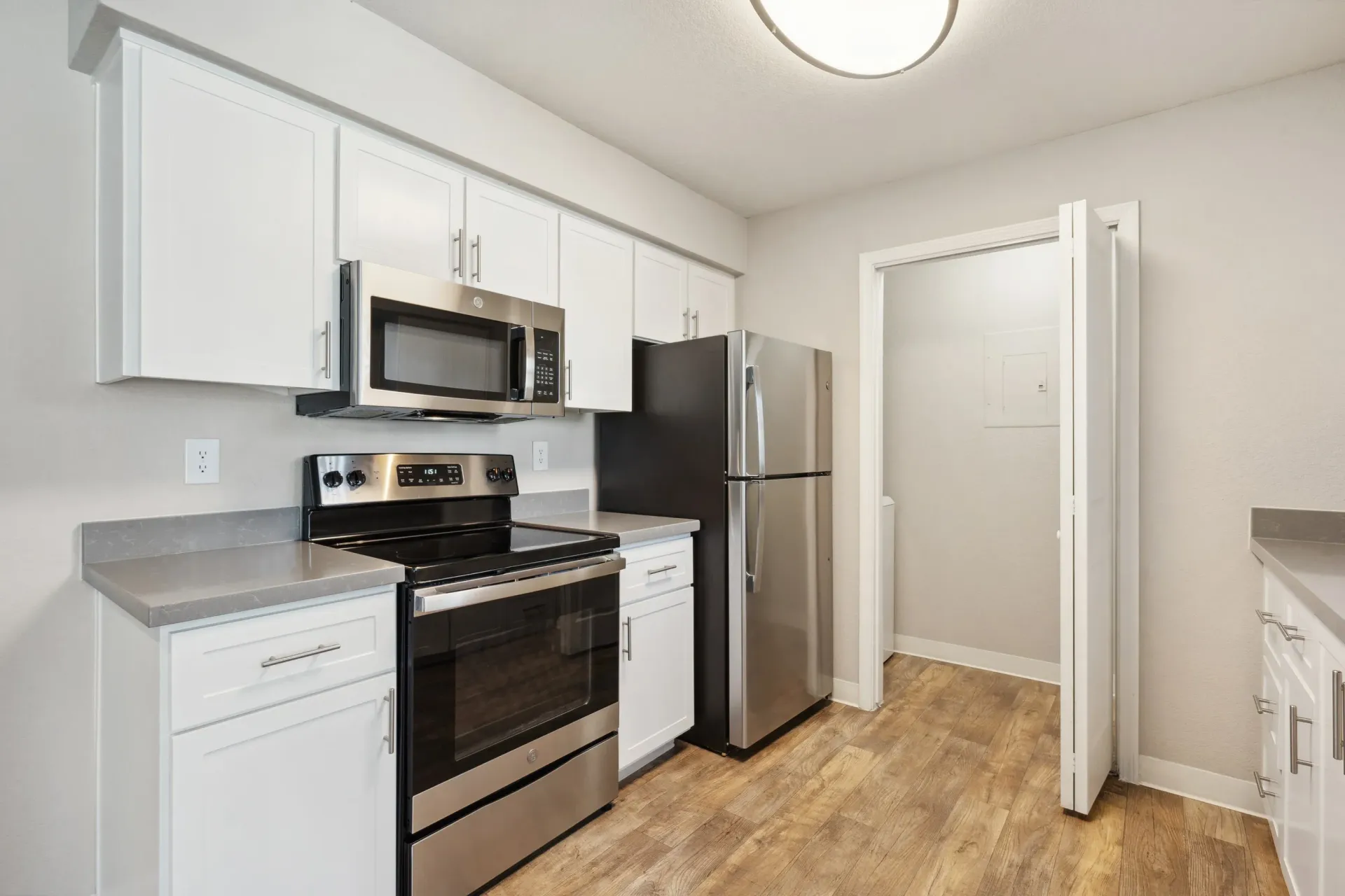 Modern apartment kitchen with white cabinets, stainless-steel appliances, and wood-look flooring.