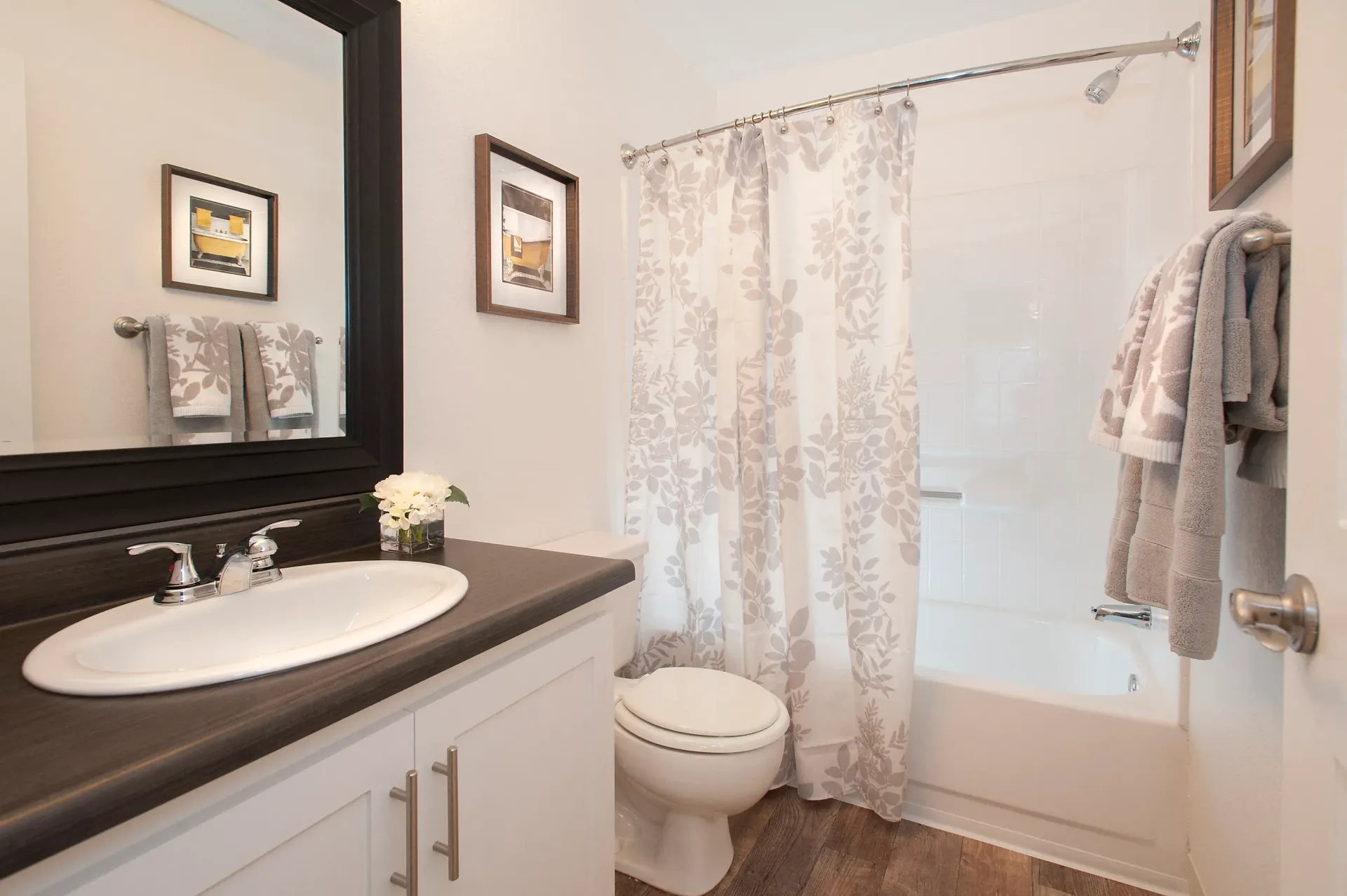 Bathroom with vanity sink, large mirror, toilet, and a tub/shower with patterned curtain.