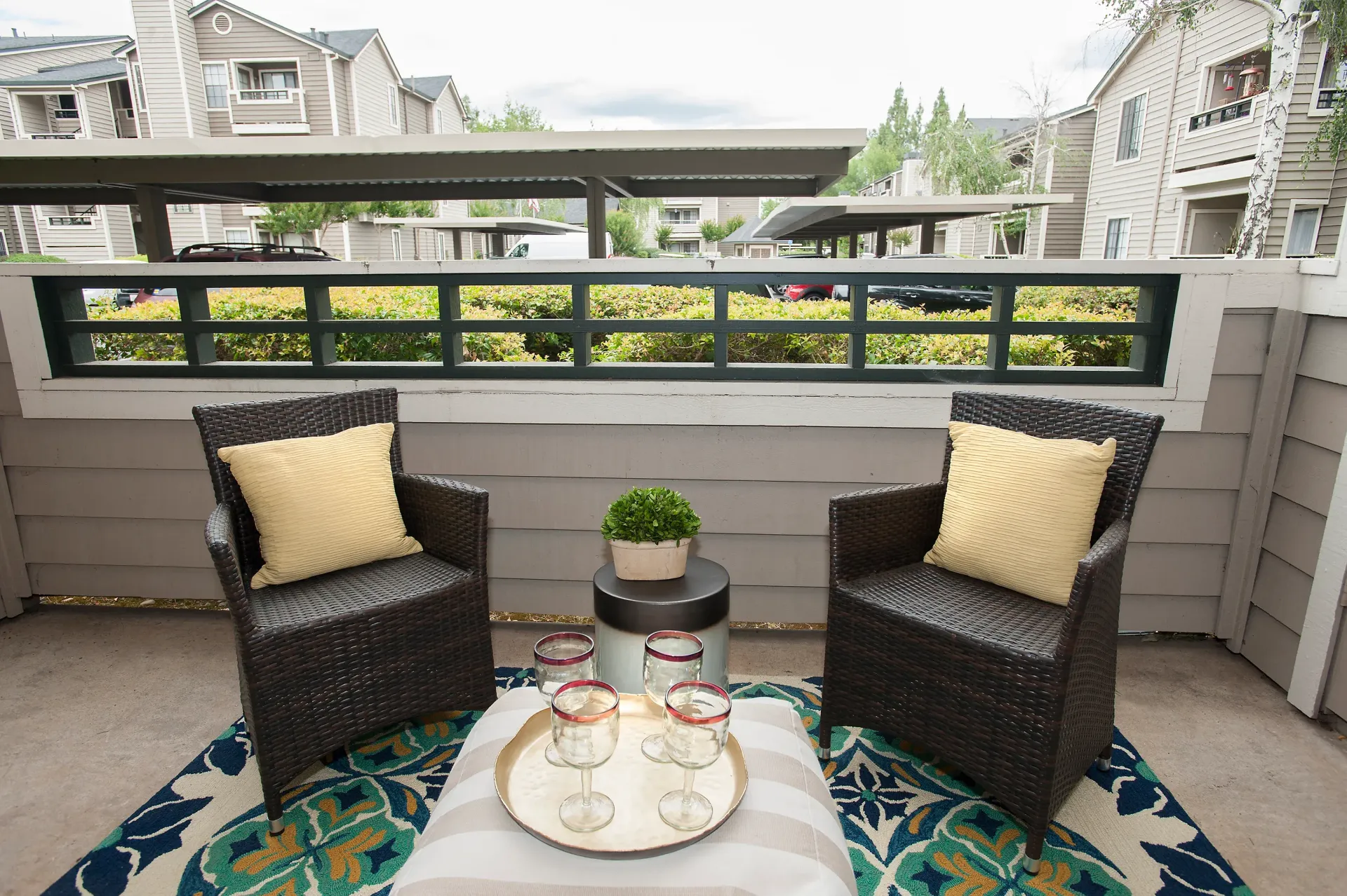 Balcony seating area with two wicker chairs and a small table in a residential community.