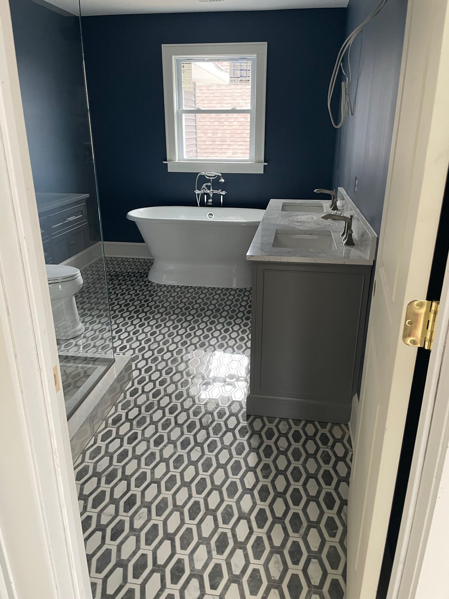 Navy bathroom with patterned tile floor, white tub, gray vanity, and window above the tub. Navy bathroom with patterned tile floor, white tub, gray vanity, and window above the tub.