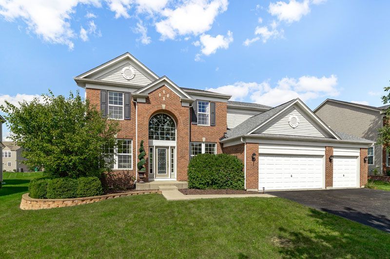 Maison en briques de deux étages avec pelouse à l'avant, garage double et ciel bleu.