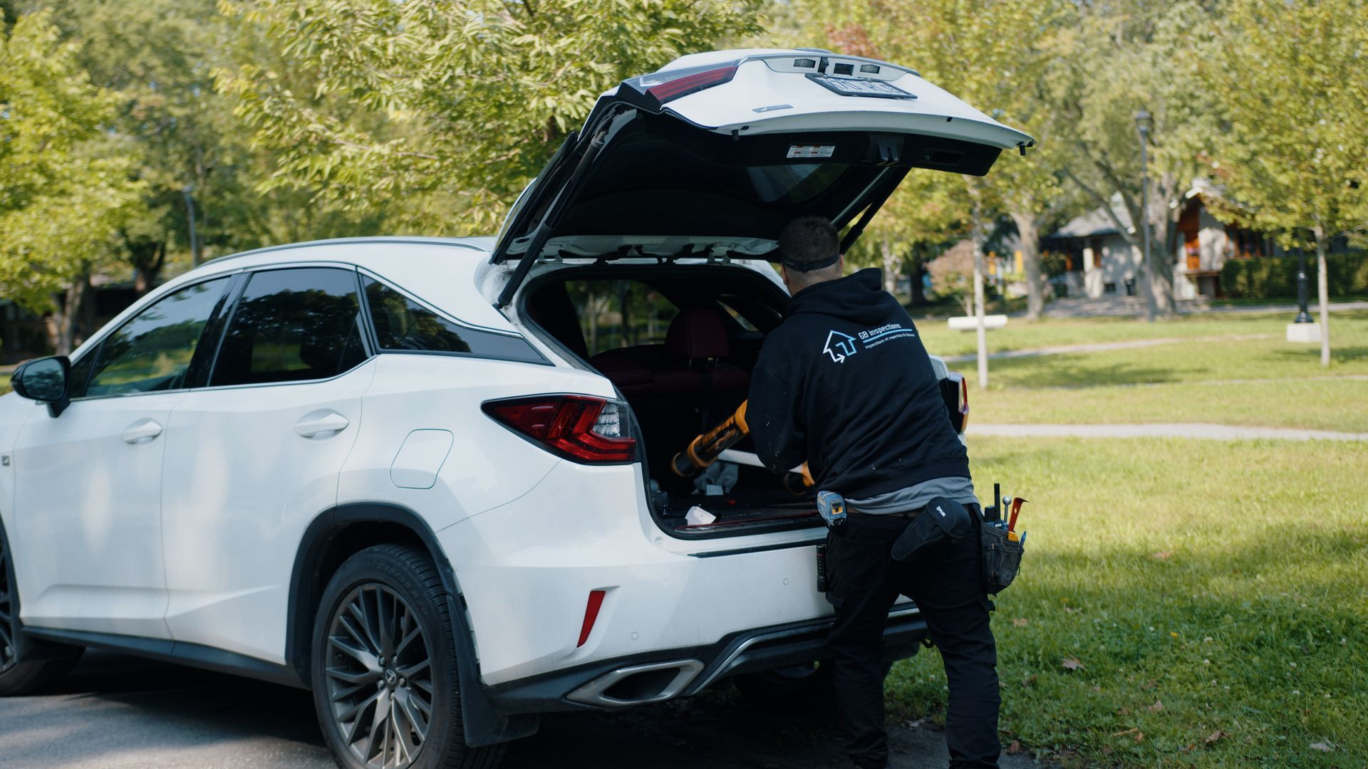 Une personne vêtue d'une veste à capuche sombre récupère du matériel dans le coffre ouvert d'un SUV blanc stationné