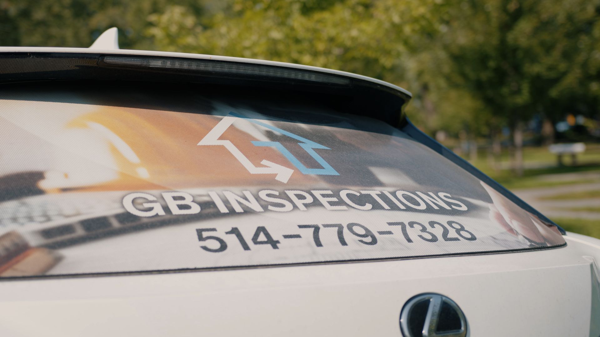 Lunette arrière blanche de voiture avec le logo « GB-INSPECTIONS » et un numéro de téléphone.