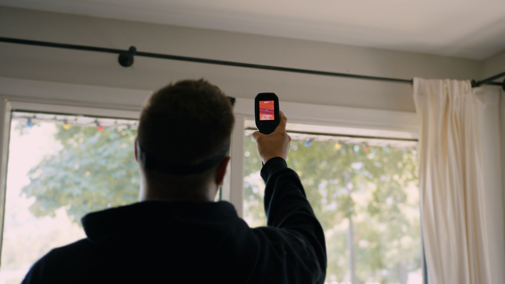 Une personne tient son téléphone devant une fenêtre, probablement en train de scanner des documents. Intérieur, rideaux visibles.