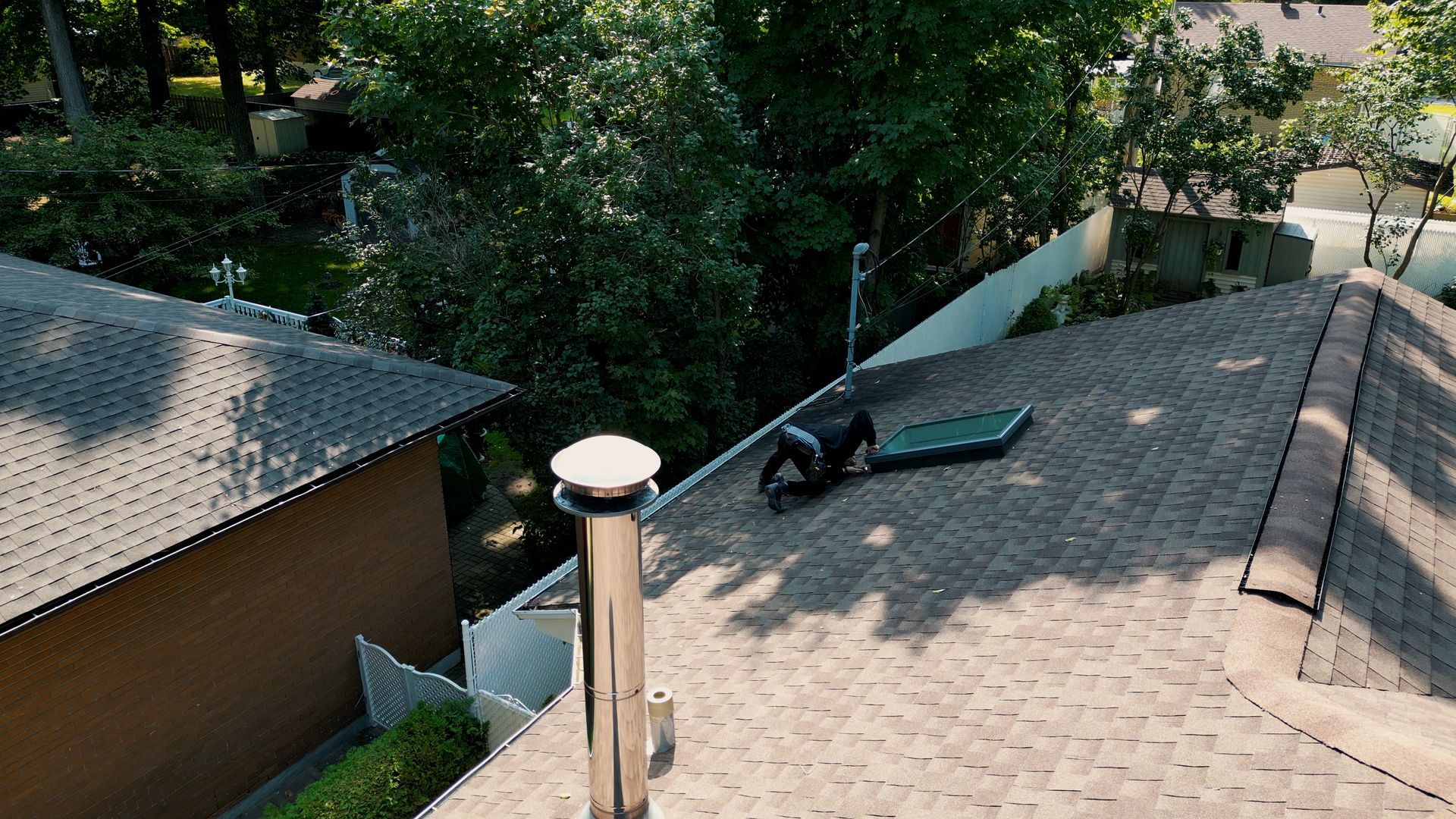 Une personne sur un toit avec un panneau solaire, près d'une cheminée et d'arbres en arrière-plan.
