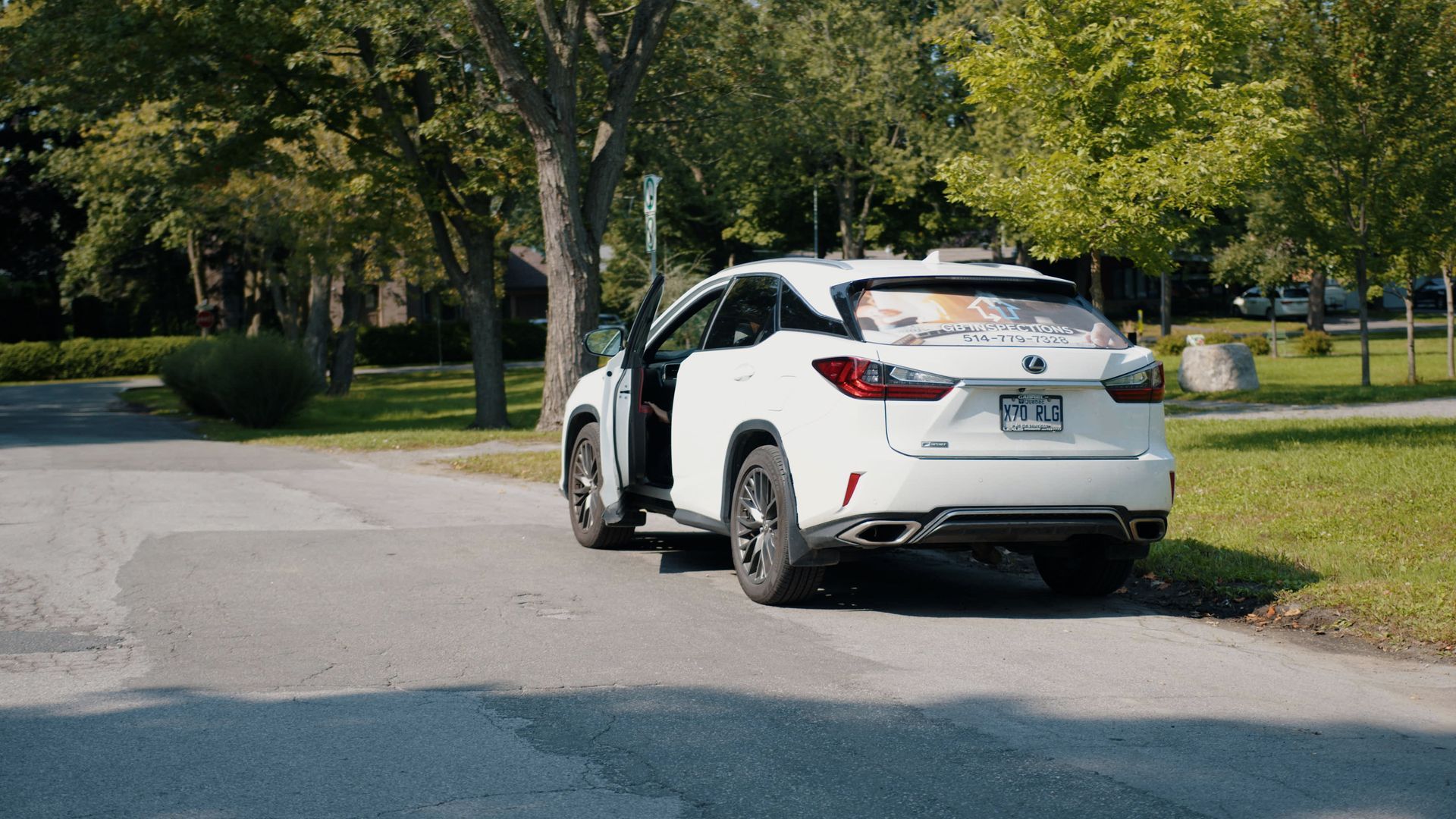 Un SUV est stationné sur une allée pavée près d'arbres et d'une pelouse, la portière côté conducteur partiellement ouverte.