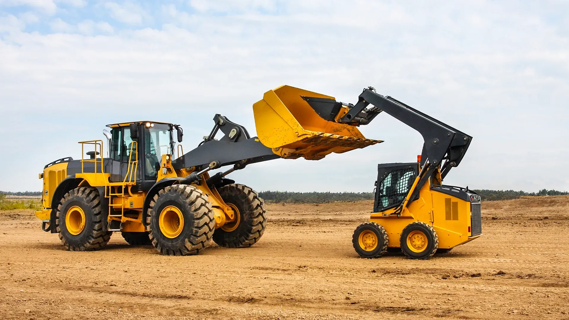 Two heavy-duty construction machines, a large front loader and a compact skid steer, positioned on a