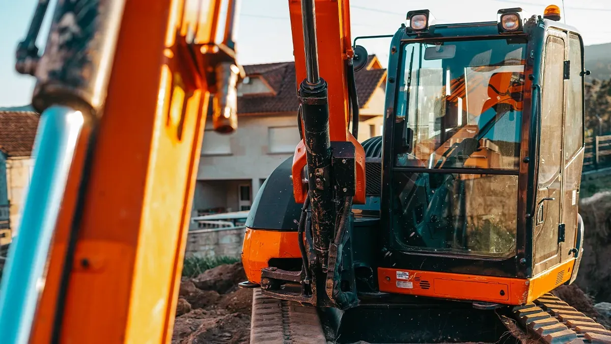 A compact mini excavator on a job site in front of residential buildings.