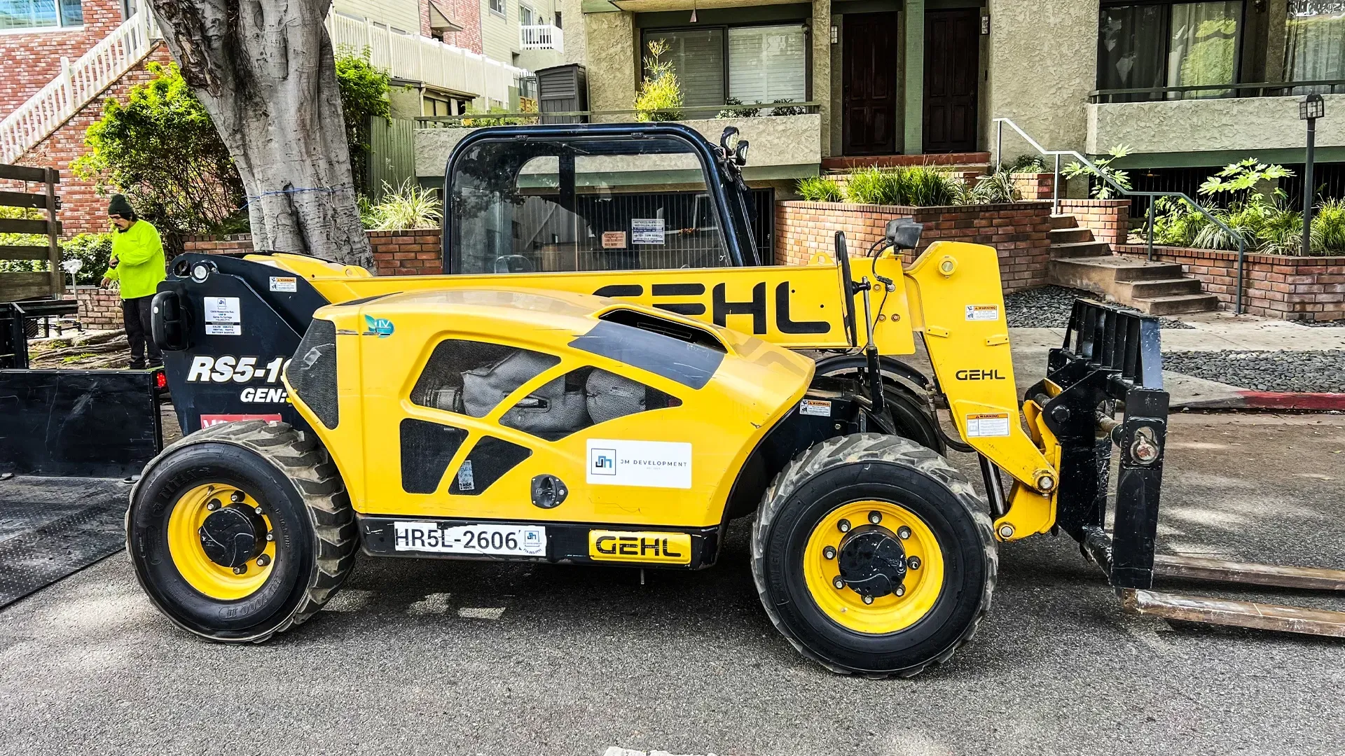 Yellow Gehl telehandler with JM Development logo parked at residential job site.