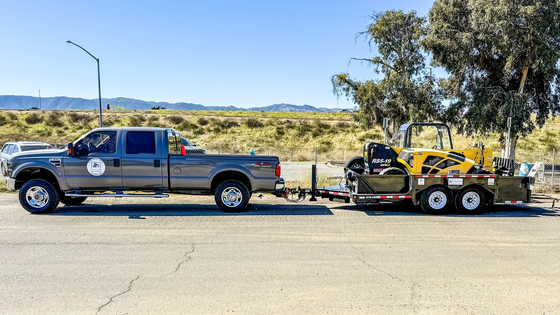 JM Development truck is towing a trailer with a yellow tractor on it.
