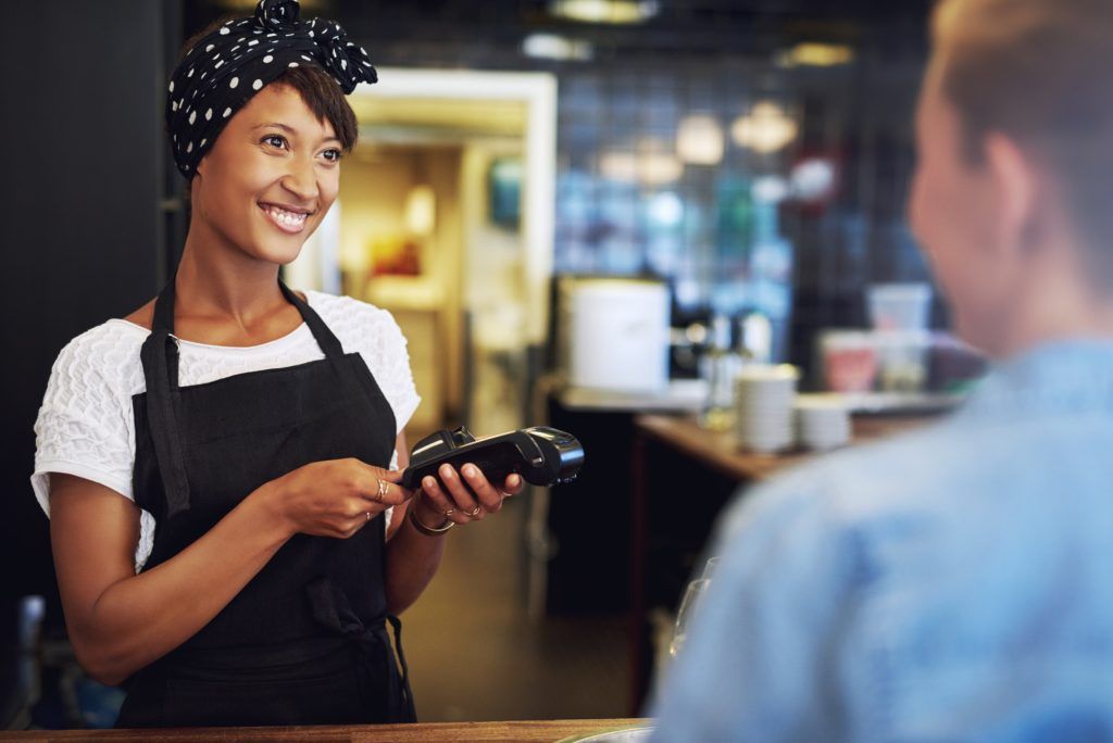 A woman in an apron is smiling while holding a credit card reader. A woman in an apron is smiling while holding a credit card reader.