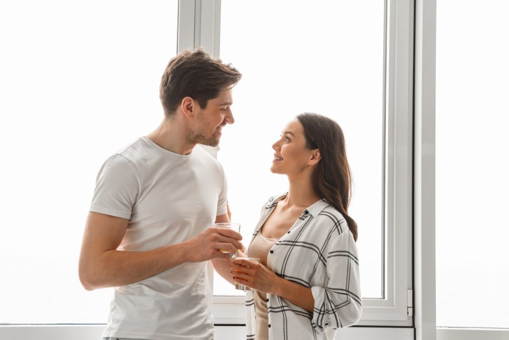 A man and a woman are standing next to each other in front of a window.