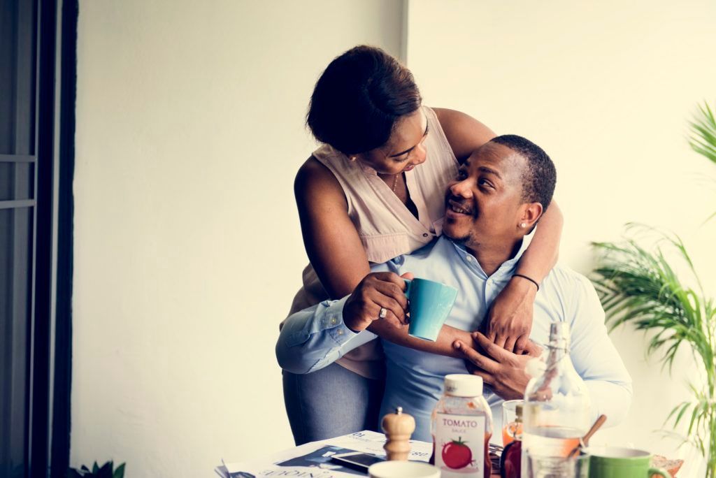 A woman is hugging a man while he holds a cup of coffee.