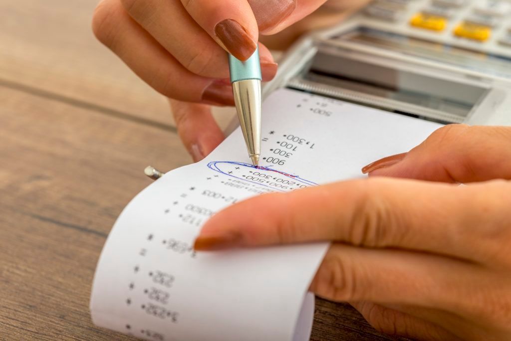 A person is writing on a receipt next to a calculator.