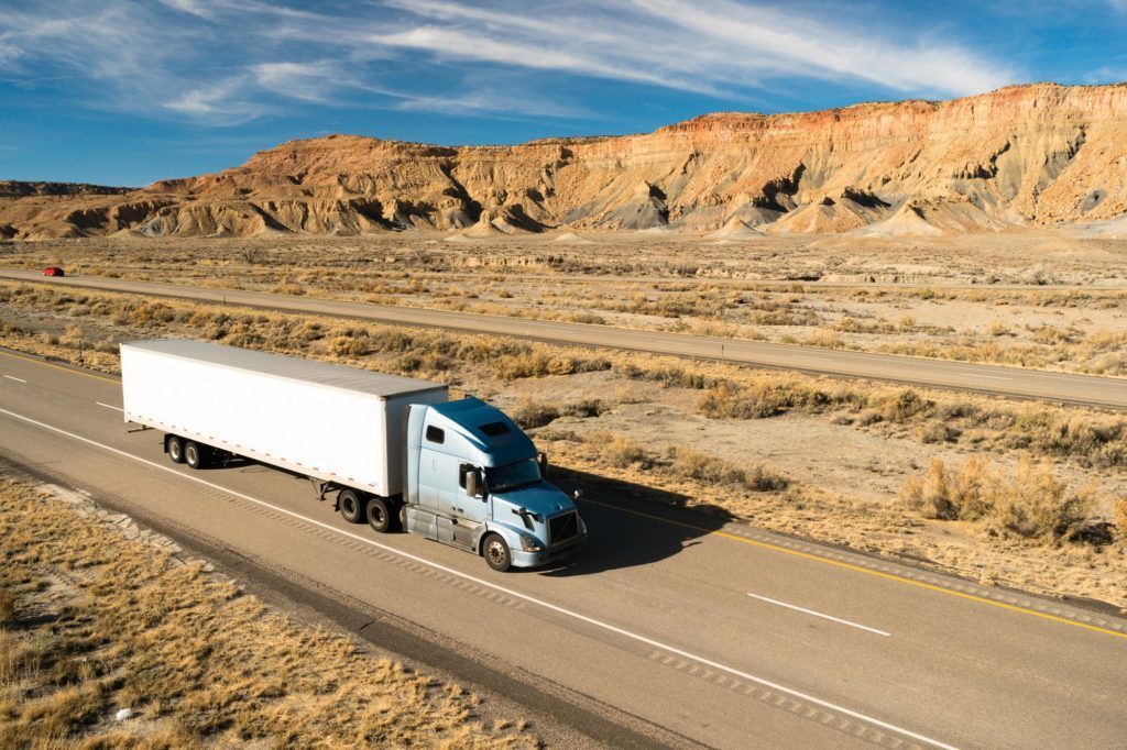 A semi truck is driving down a desert road.