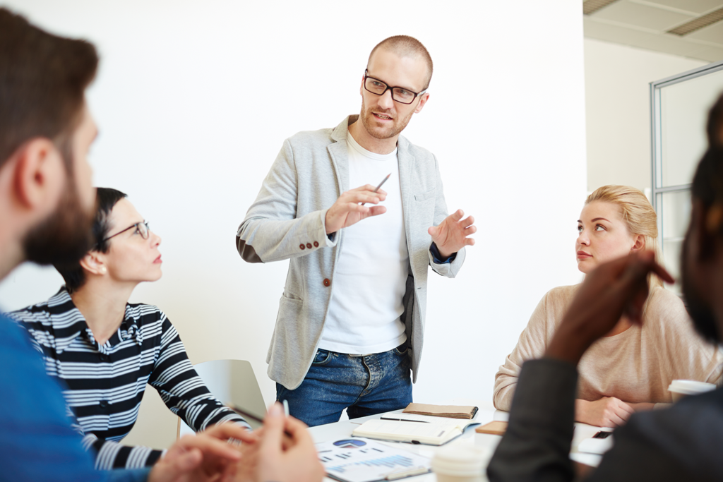 A man is giving a presentation to a group of people sitting around a table.